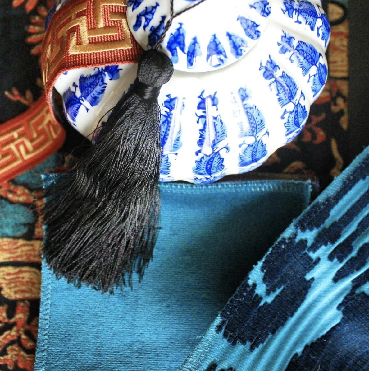 Close-up of a graduation tassel hanging from a cap with intricate blue and white patterns, resting on a textured blue fabric with a patterned rug background.