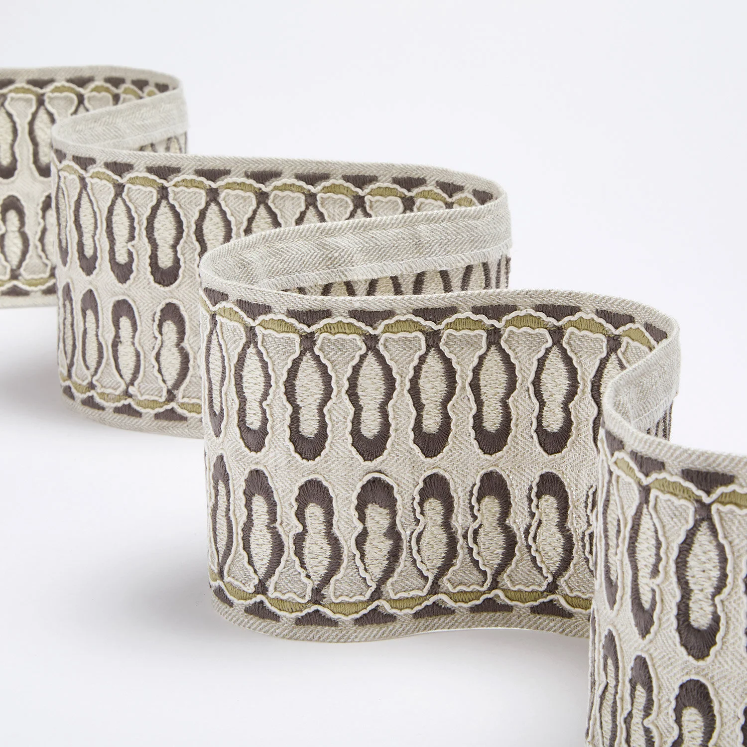 A close-up of embroidered fabric ribbons with intricate patterns in beige, brown, and olive green styles displayed in a wavy arrangement.