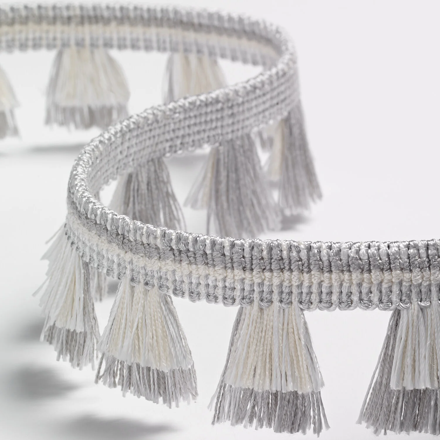 Close-up image of a silver and white metallic tassel fringe trim, with multiple tassels hanging from a woven band.