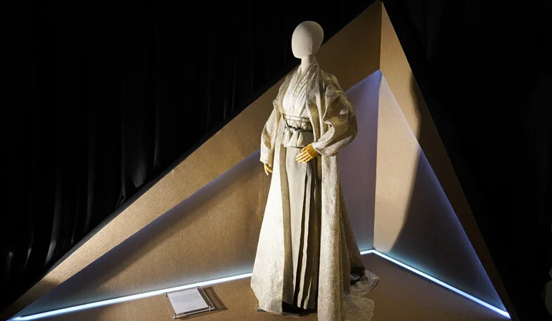 A mannequin dressed in traditional Japanese clothing displayed on a stage with geometric walls and a black curtain backdrop.