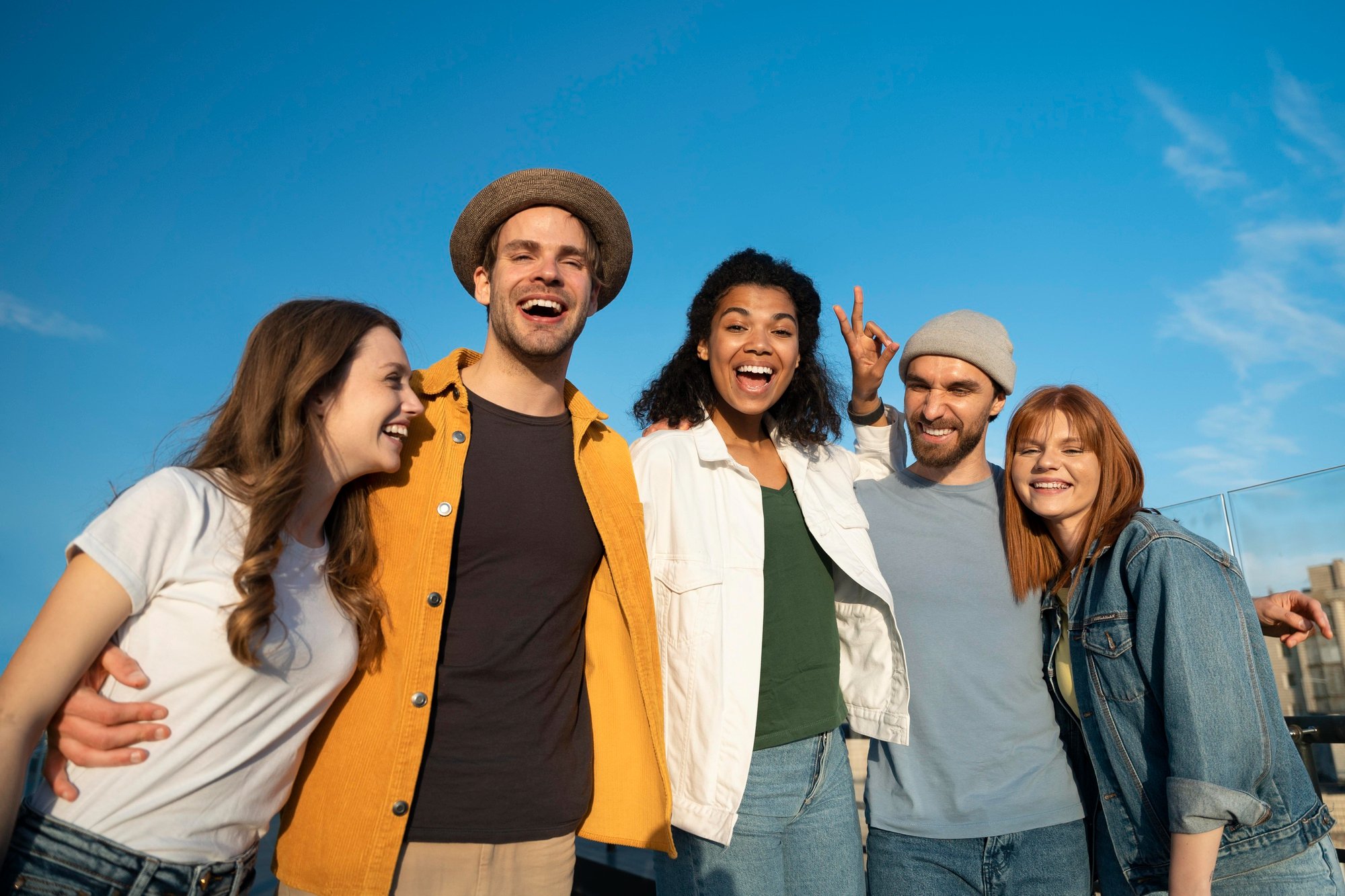 Group of five friends smiling and enjoying each other's company outdoors on a sunny day.