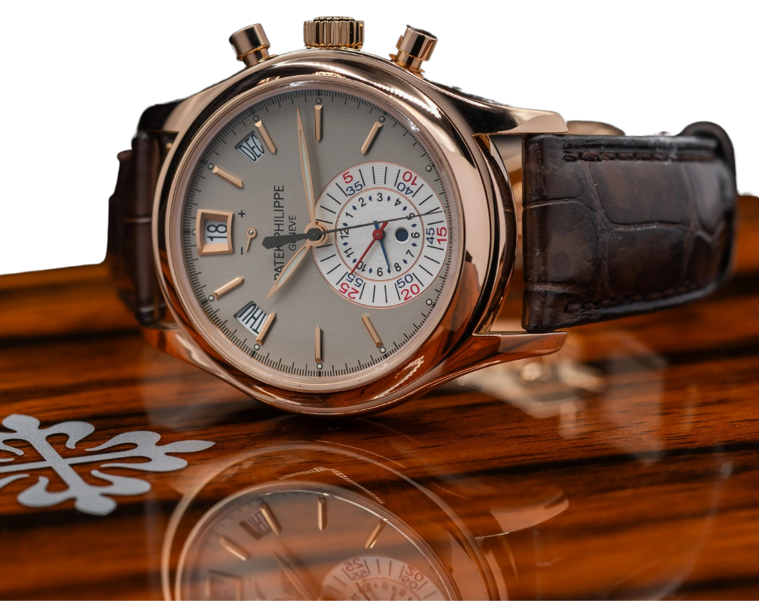 Close-up of a luxury wristwatch with a white dial, gold case, black leather strap, and multiple sub-dials, resting on a wooden surface.