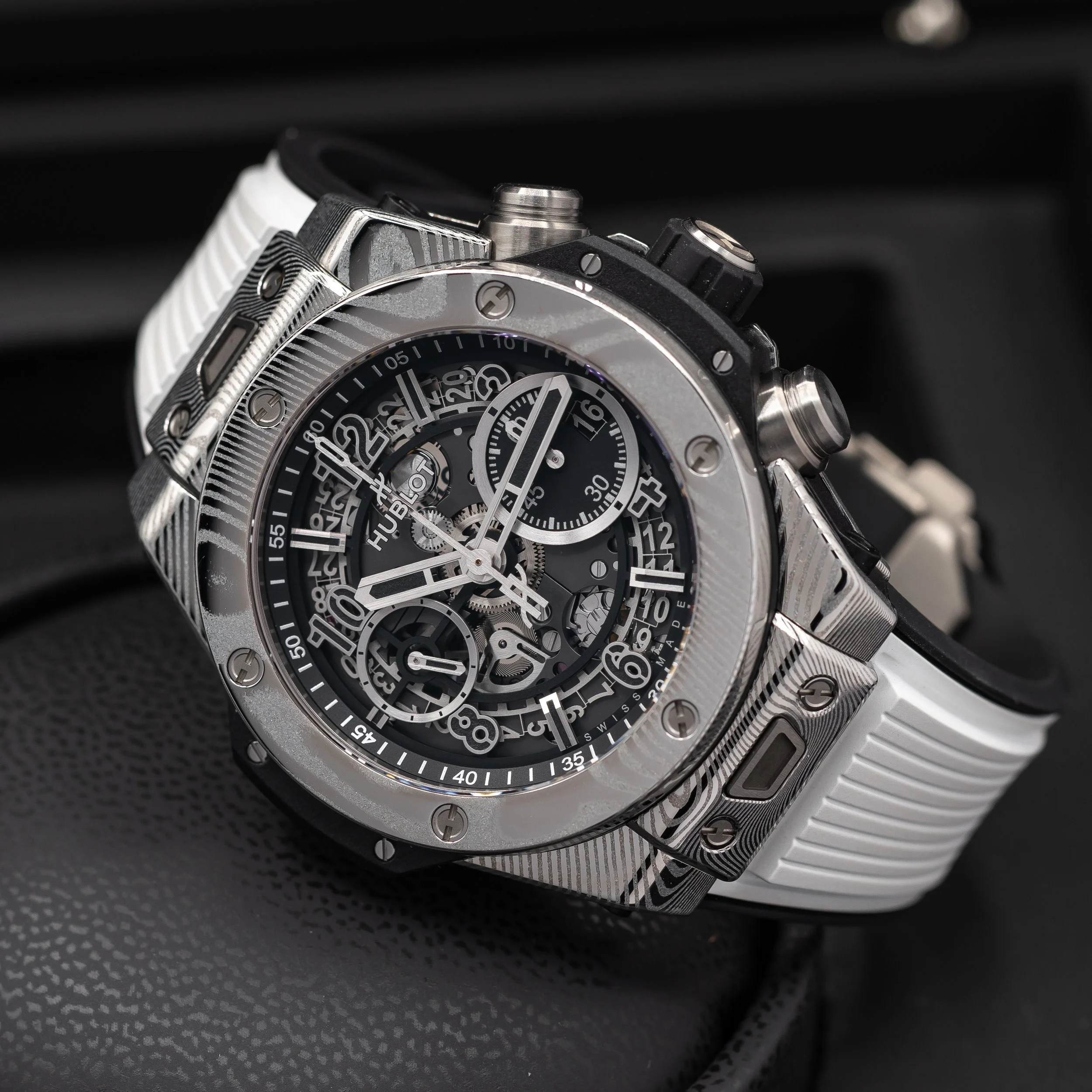 A detailed close-up of a luxury wristwatch with a black dial, skeleton design, and multiple subdials, featuring a white strap and a silver casing.