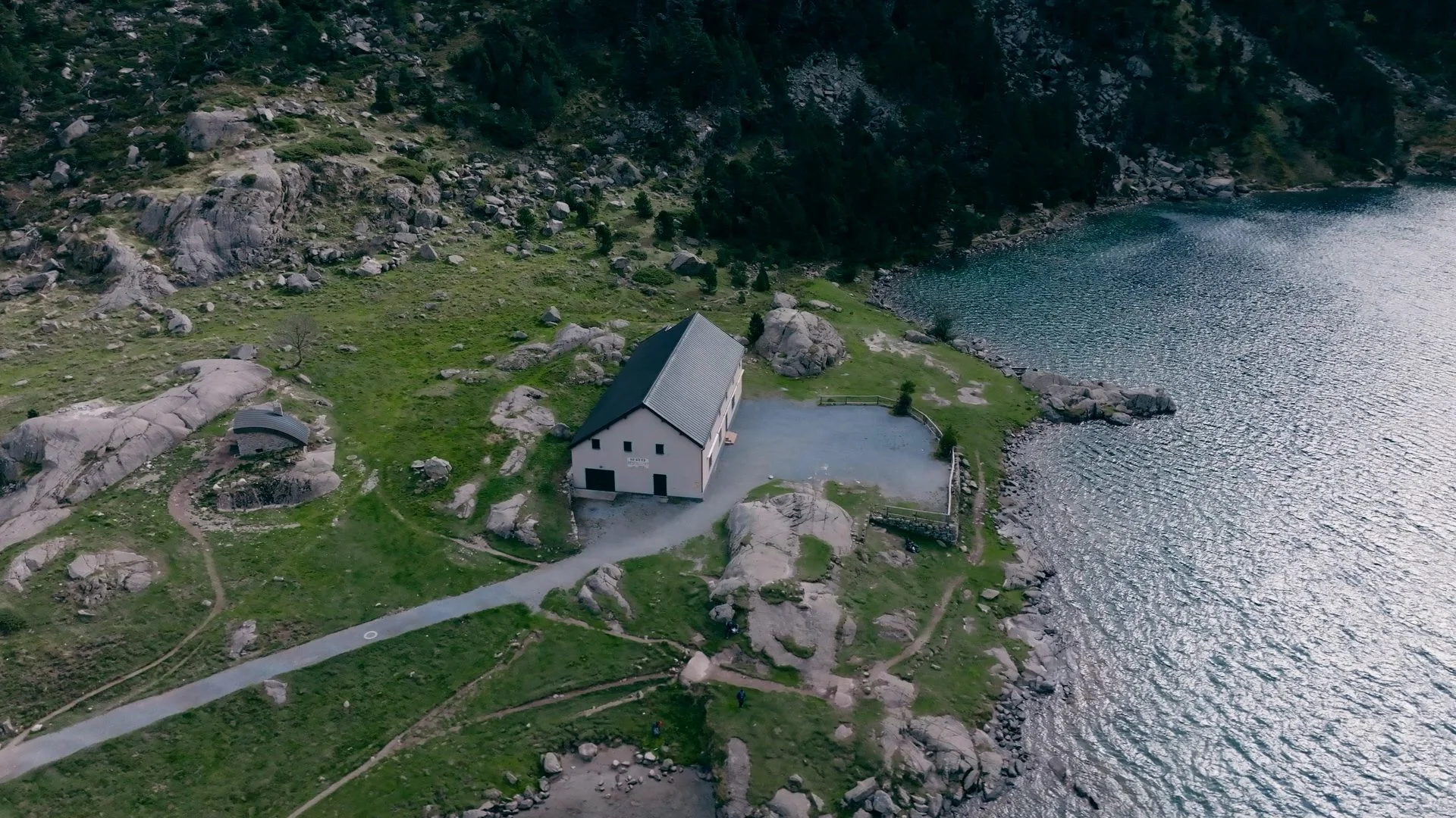 Une maison en bois au bord d'un lac entourée de montagnes et de rochers, lac de Gaube, région Occitanie Tourisme.