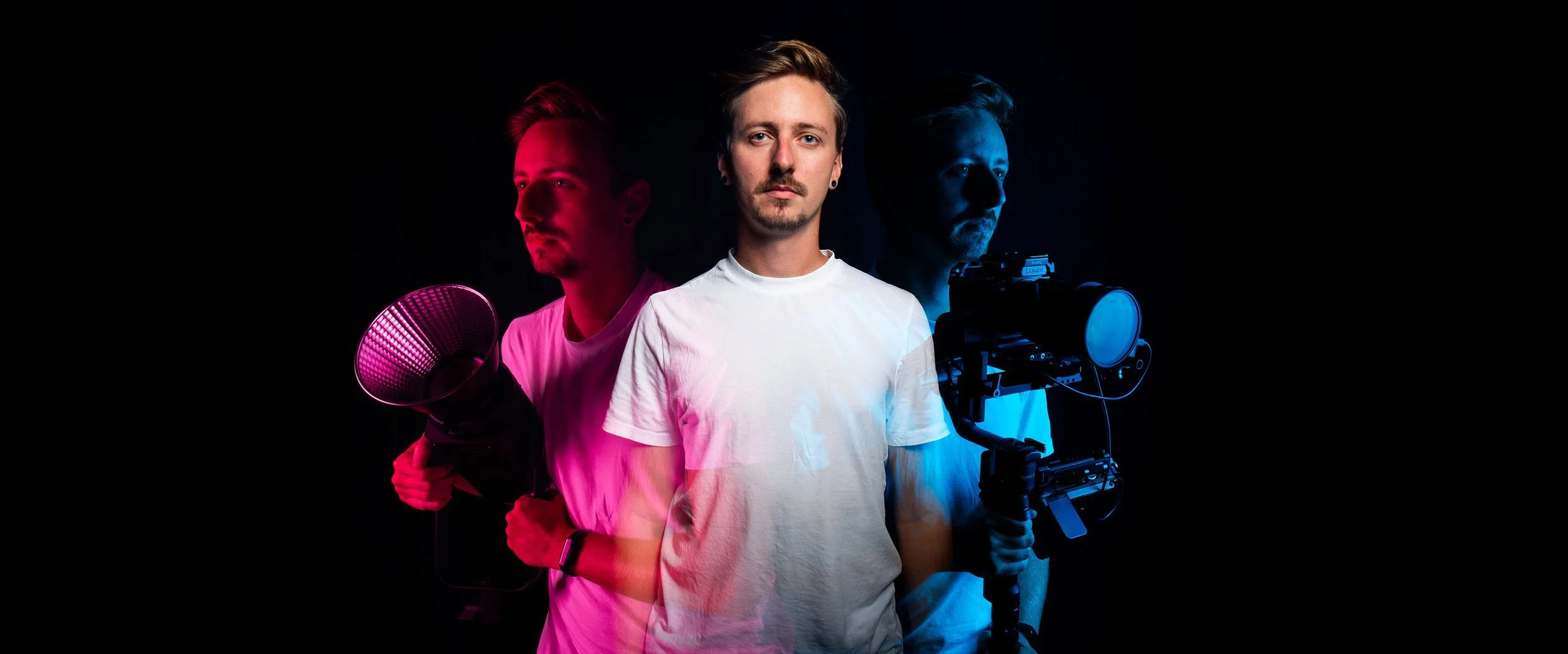 Un homme avec une chemise blanche, photographié en portrait, entouré de deux autres hommes avec des équipements de tournage, dans un contexte artistique avec un éclairage coloré rouge et bleu.