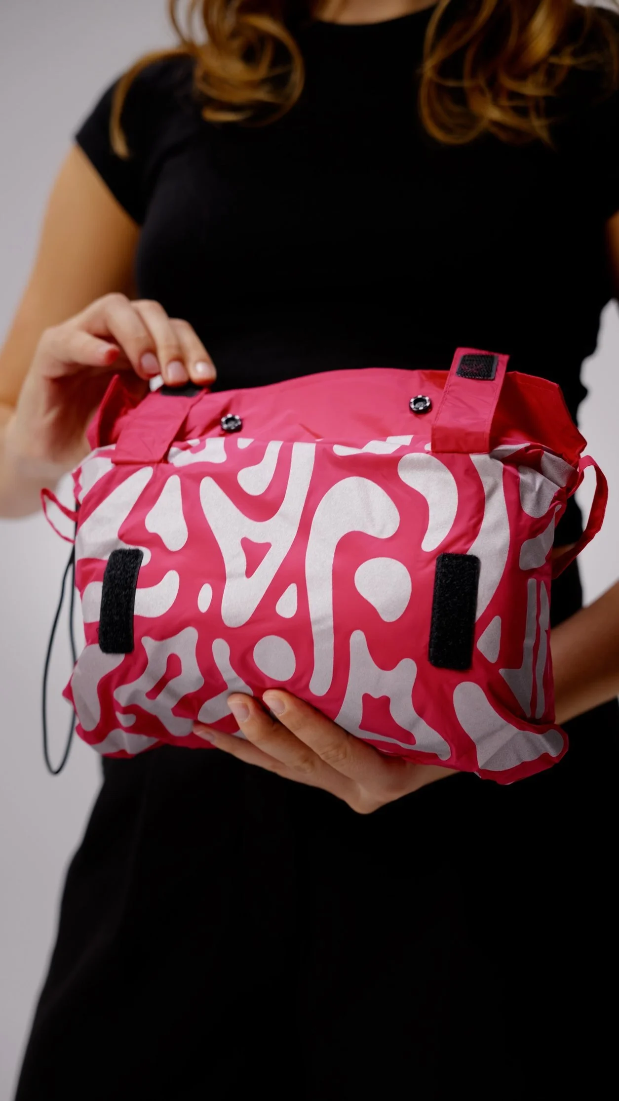 Une femme tient un sac de couleur rose avec un motif blanc et des détails en velcro noir.