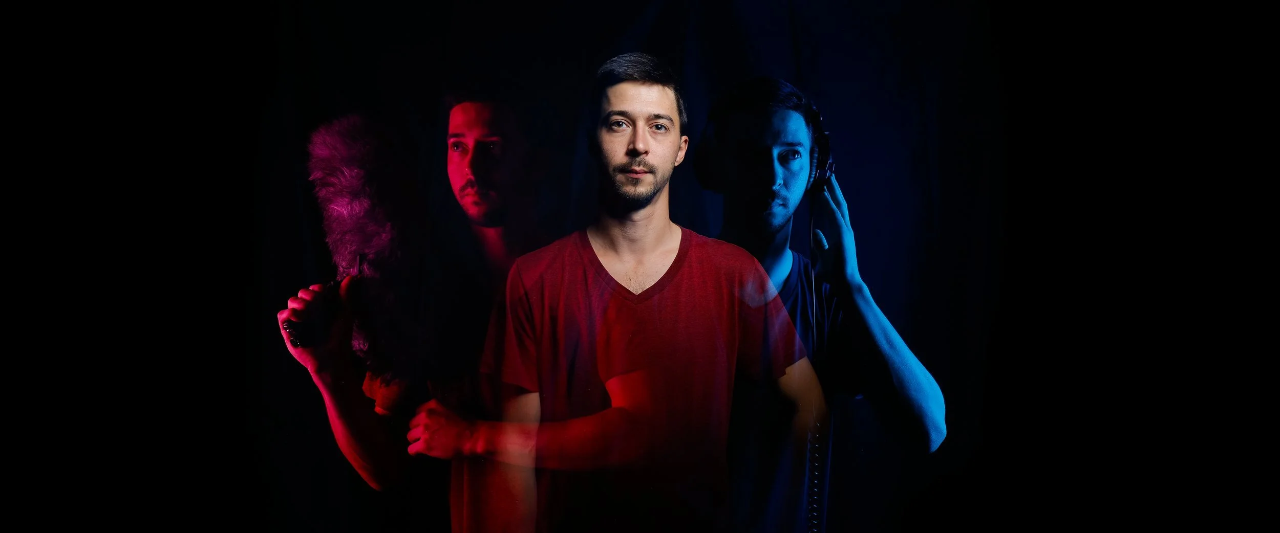 Un groupe de trois jeunes hommes, avec un éclairage rouge sur la gauche et bleu sur la droite, dans un studio sombre, un portant un casque audio et l'autre tenant un micro.