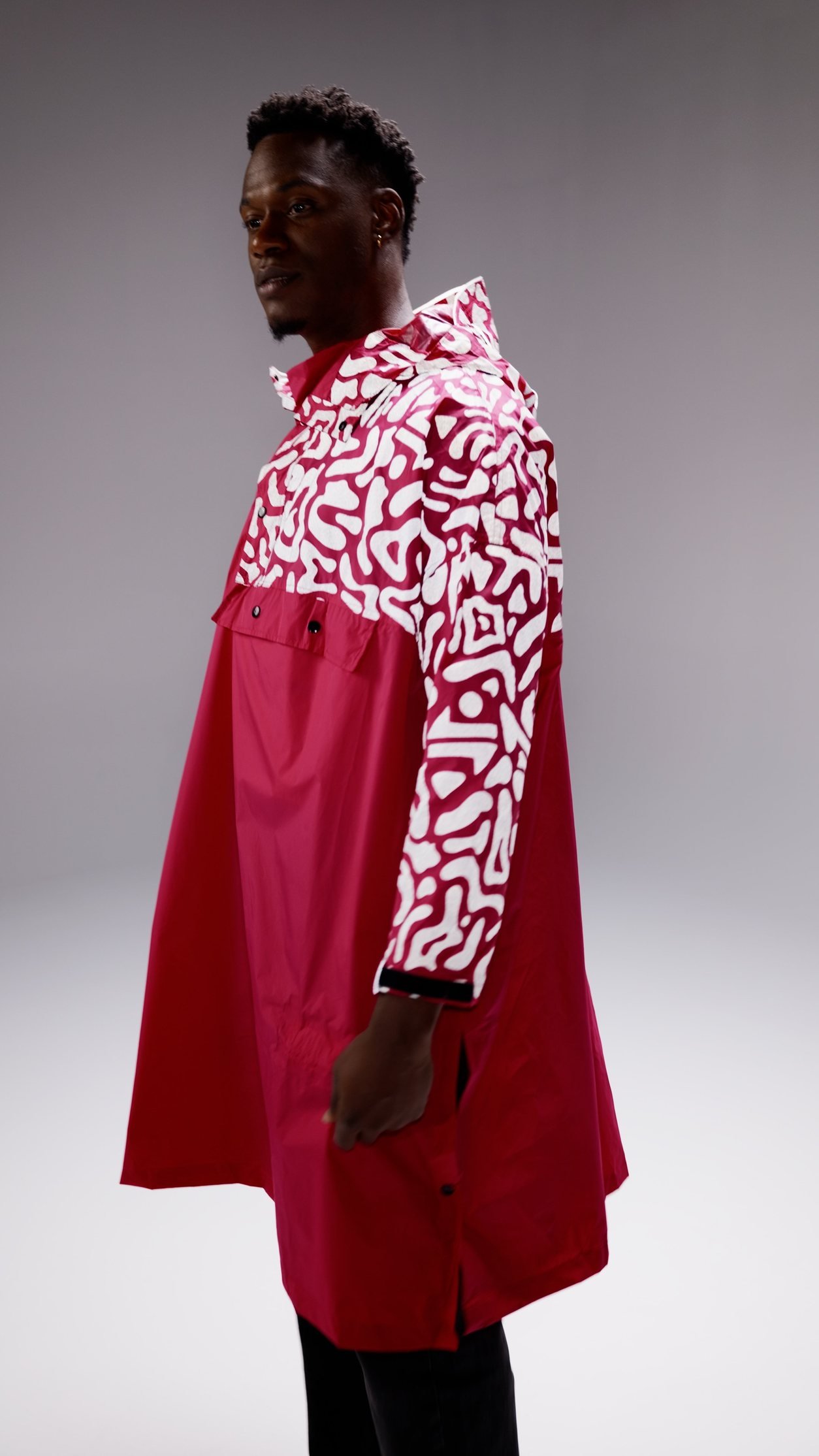 Homme portant un manteau rouge avec des manches imprimées en blanc et noir, dans un studio avec fond gris.