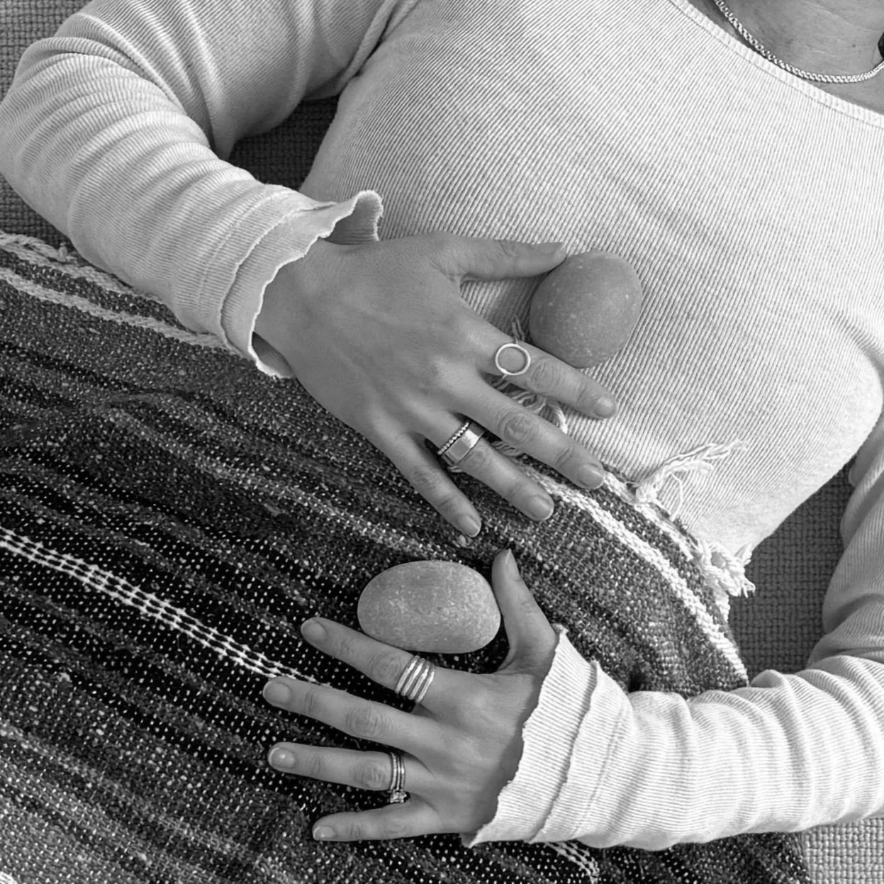 Woman laying on her back with hands on chest and belly next to ocean stones