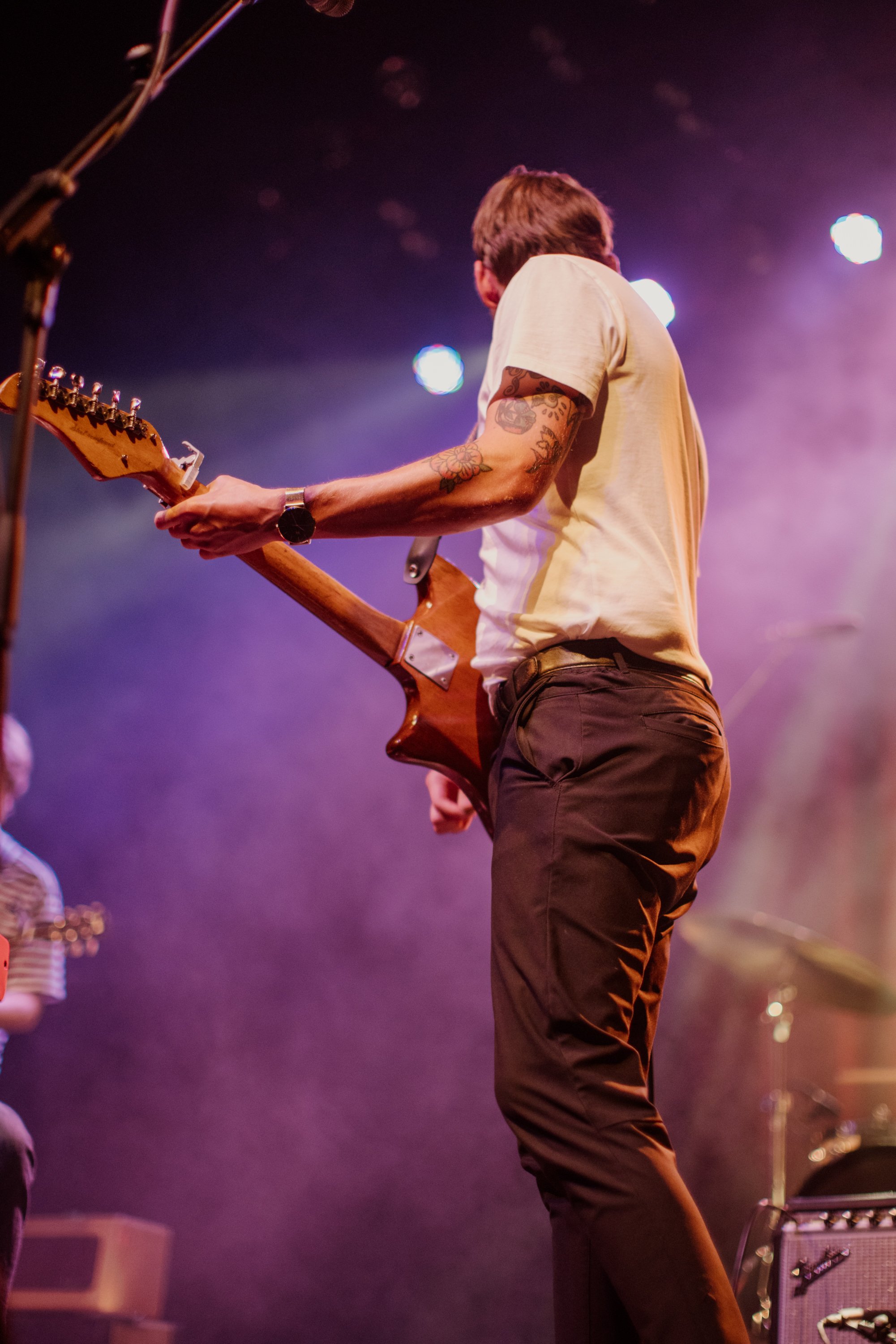 A musician playing an electric guitar on stage during a performance, with stage lights creating a colorful atmosphere.