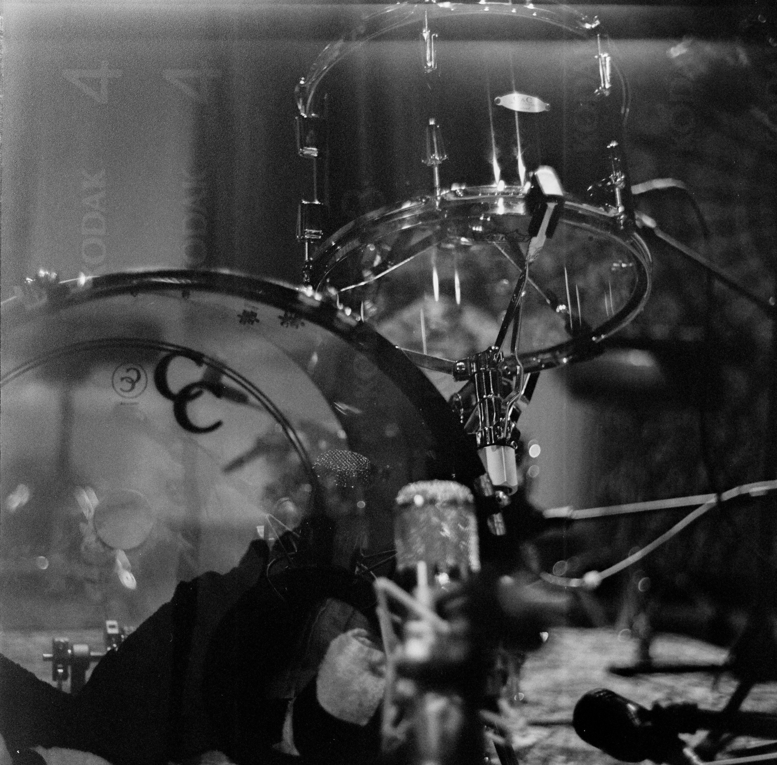 Close-up of a vintage drum set viewed through a glass window, with a microphone in the foreground and reflections on the glass.