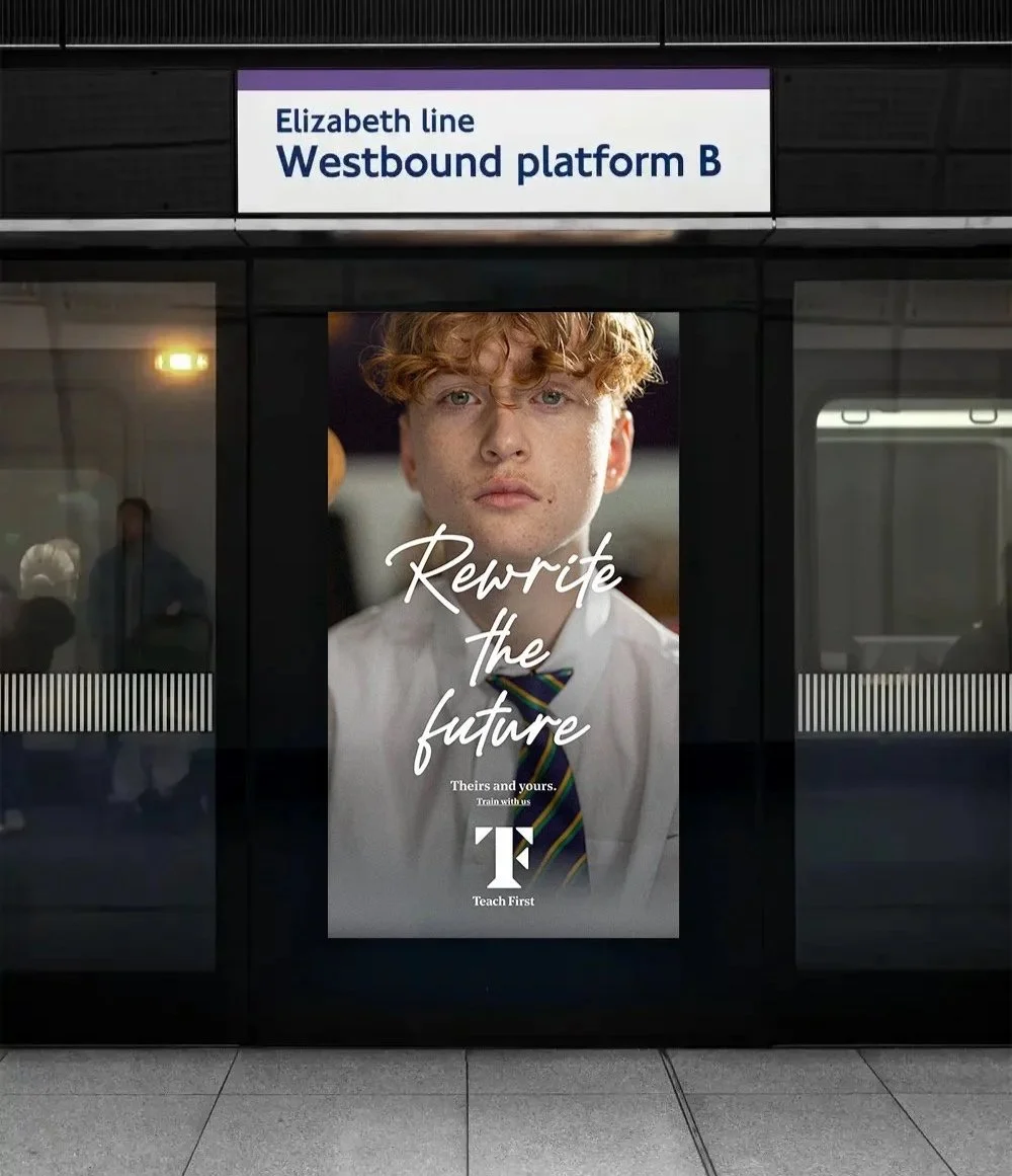 Advertisement at a train station promoting Teach First with a portrait of a young man with curly red hair, wearing a white shirt and a dark striped tie, with the slogan "Rewrite the future" and a sign at the top indicating the train line to Elizabeth Line Westbound Platform B.