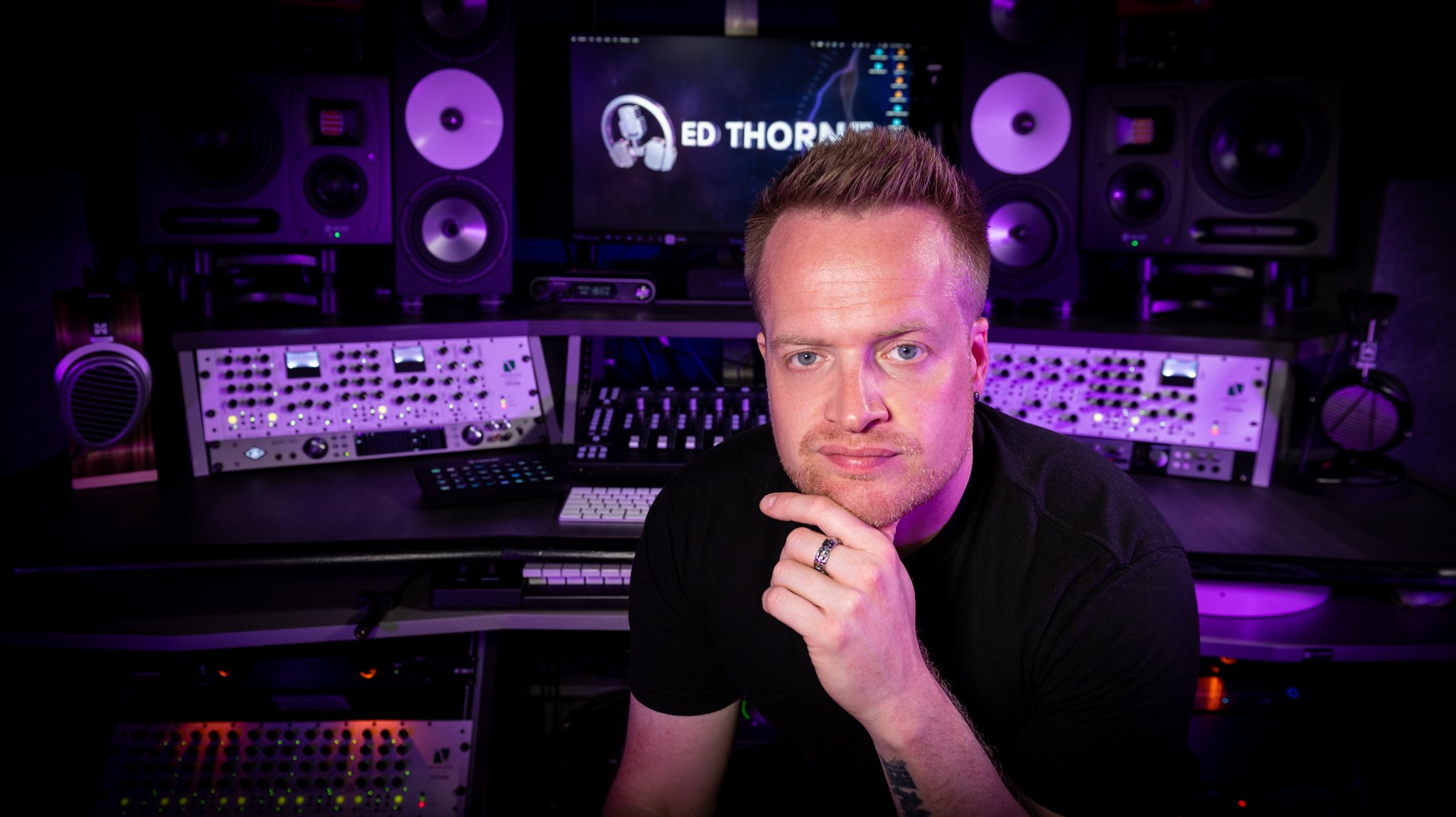 A man with short blond hair and a ring on his finger sits in a recording studio surrounded by audio equipment, including speakers, mixing consoles, and a computer monitor displaying the name Ed Thorne.
