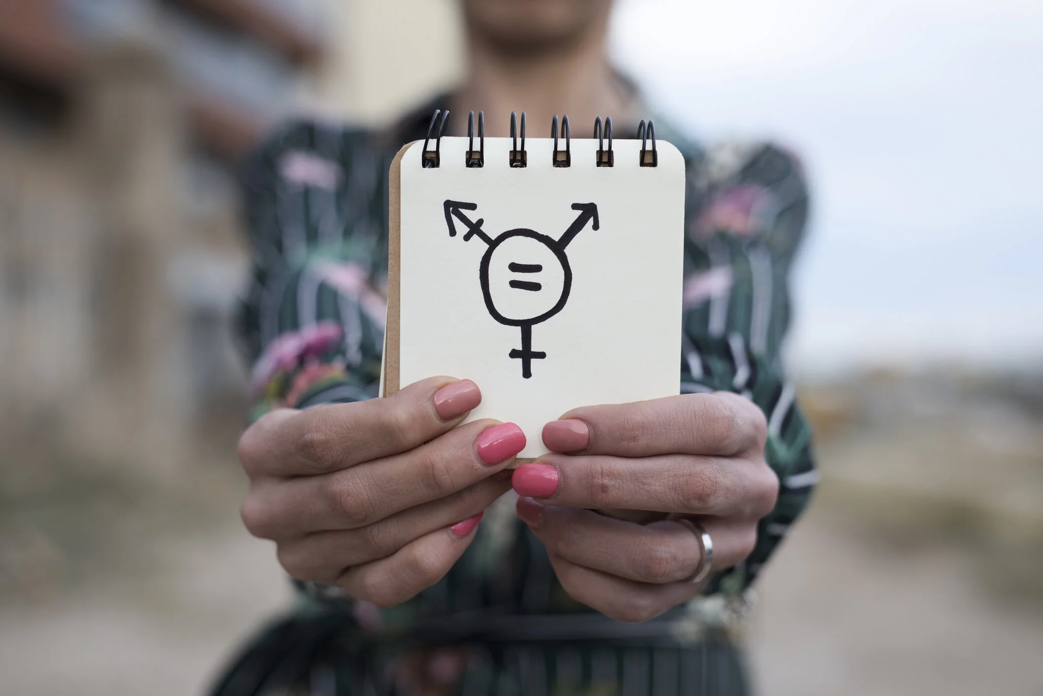 An image of a person holding up a drawing of a trans symbol illustrating trans therapy topics such as coming out as trans or coping with transphobia