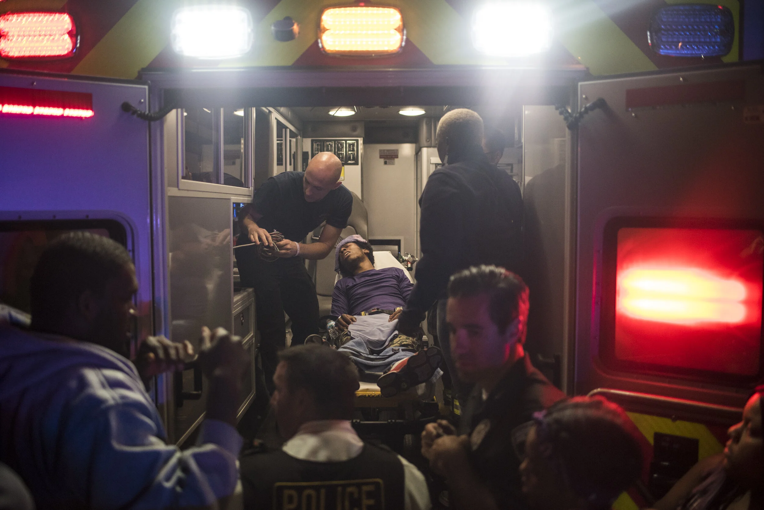 Emergency medical responders attending to a patient inside an ambulance at night, with police officers nearby.