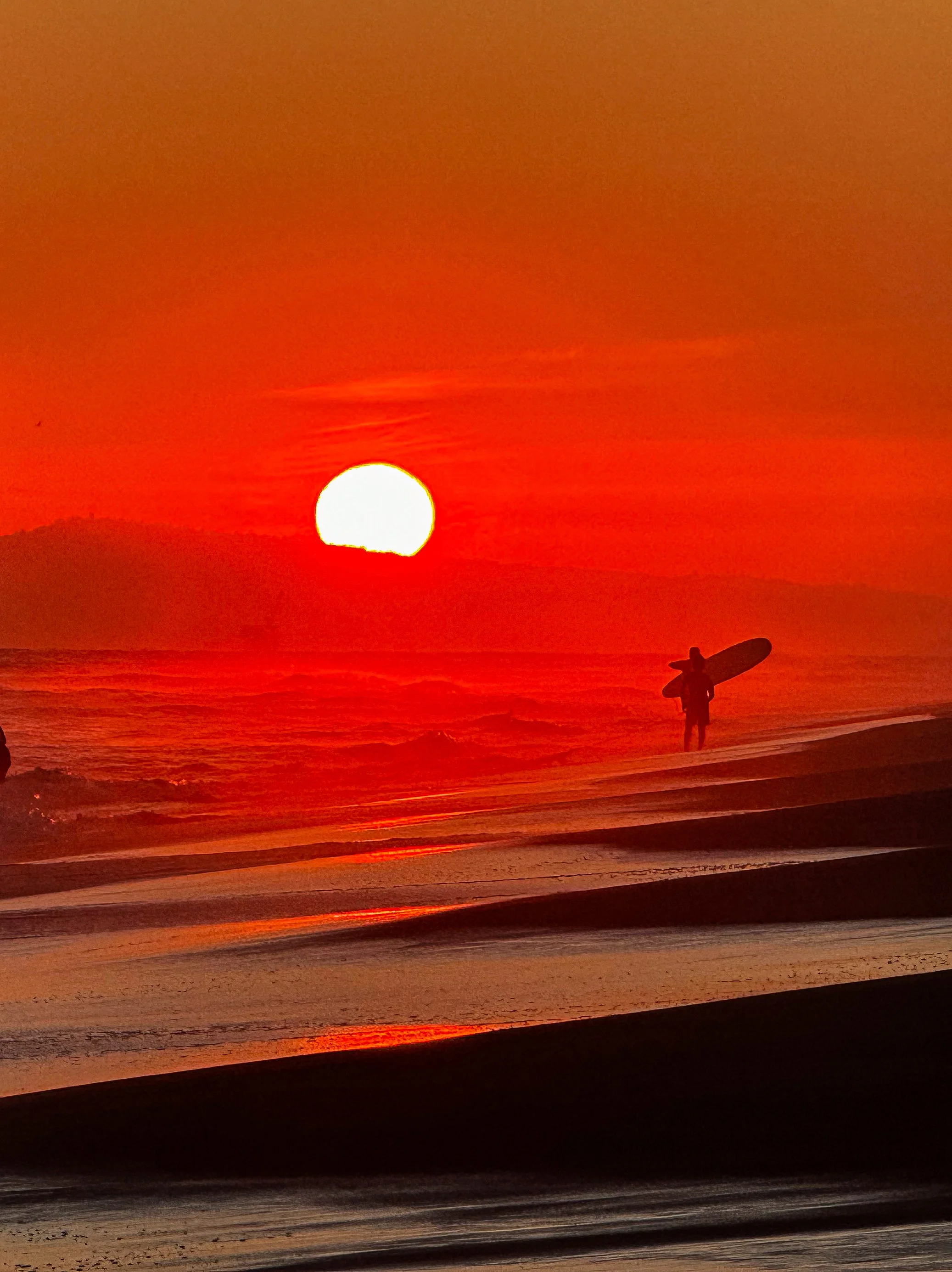 Surfers at sunset with surfboards on beach with setting sun on California beach