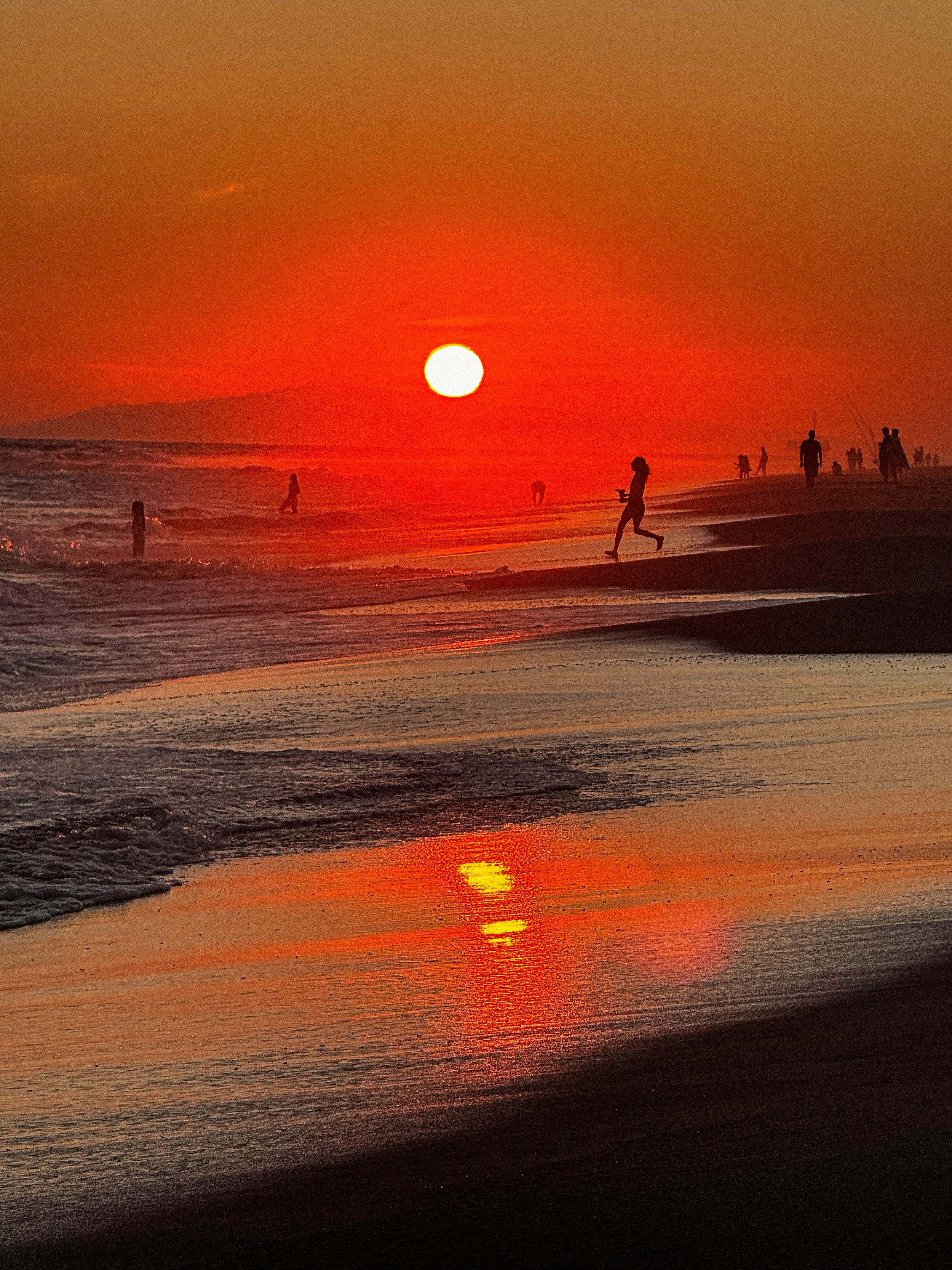 Beachgoers in Southern California beach with sun setting over sand and ocean waves crashing