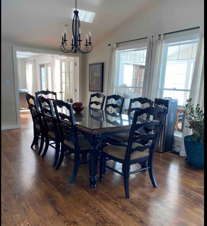 Dining room with rectangular glass table, black wooden chairs, chandelier, and hardwood floor.