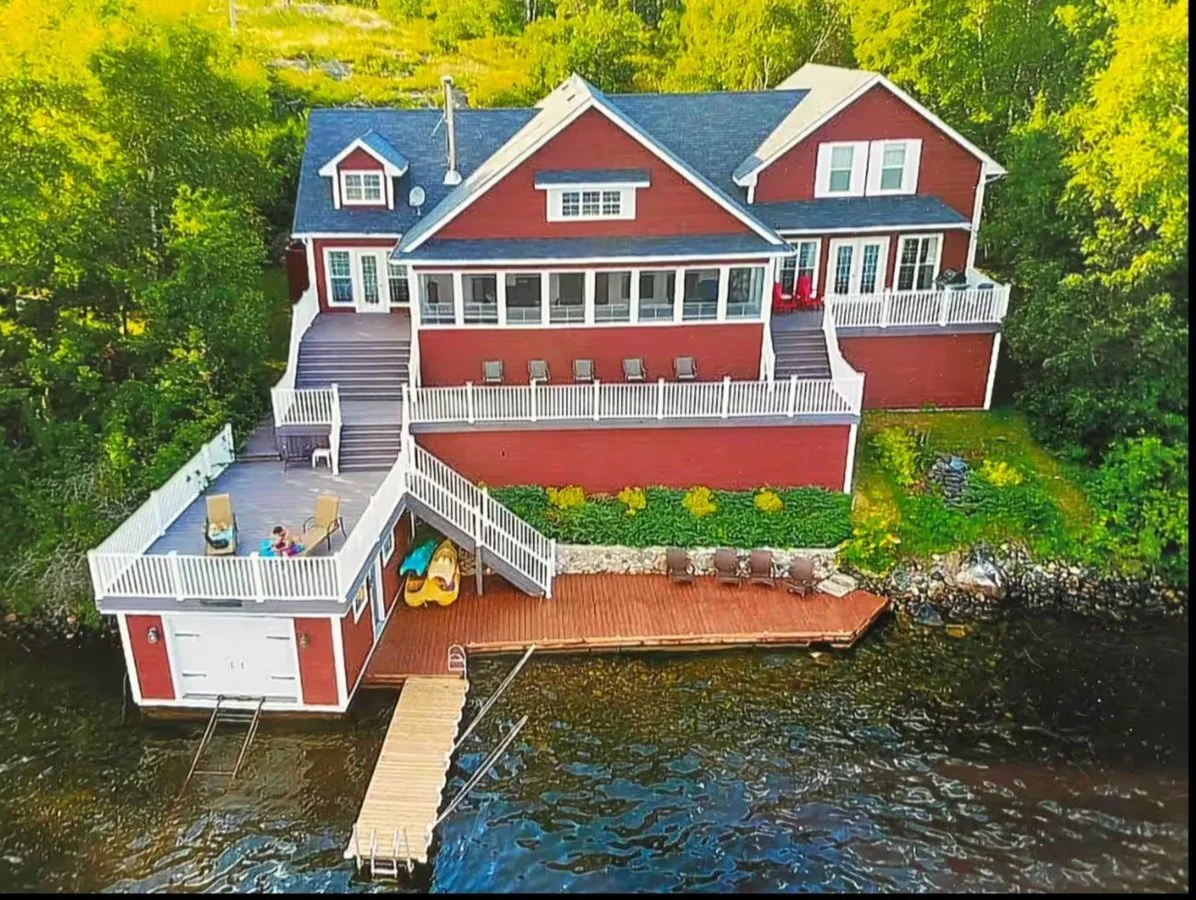 Lakeside house with red siding, multiple decks, and dock on the water