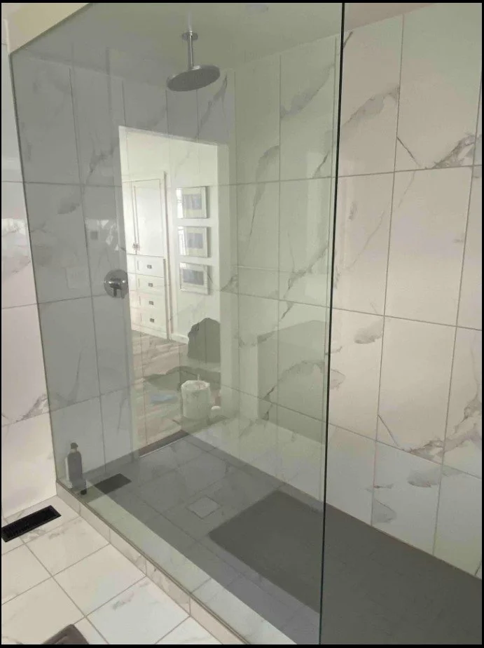 Modern bathroom shower with glass enclosure, marble tile walls, and ceiling-mounted showerhead.