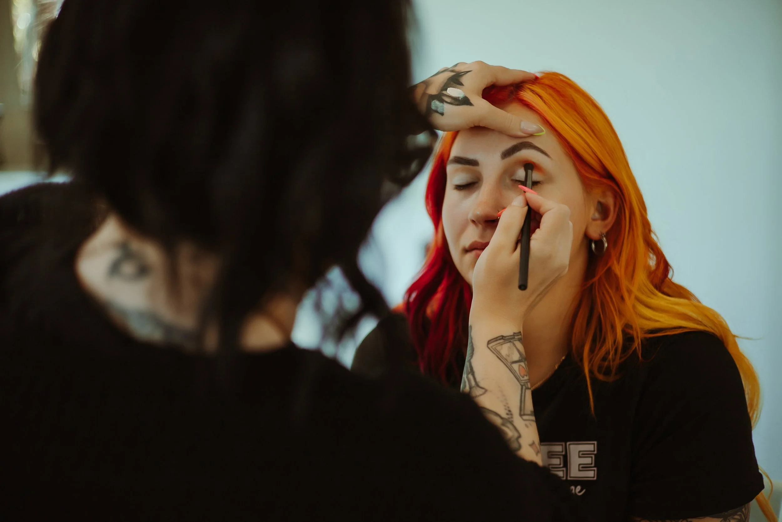 Makeup artist applying eyeshadow on a person with red and orange hair.