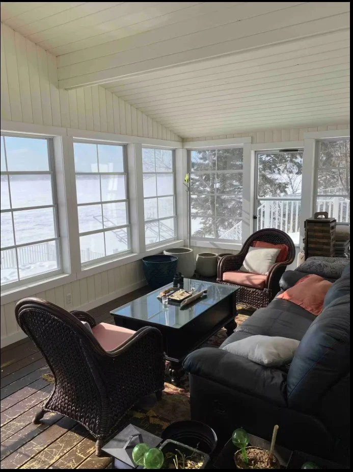 Sunroom with wicker furniture, glass coffee table, and large windows revealing a snowy outdoor view.