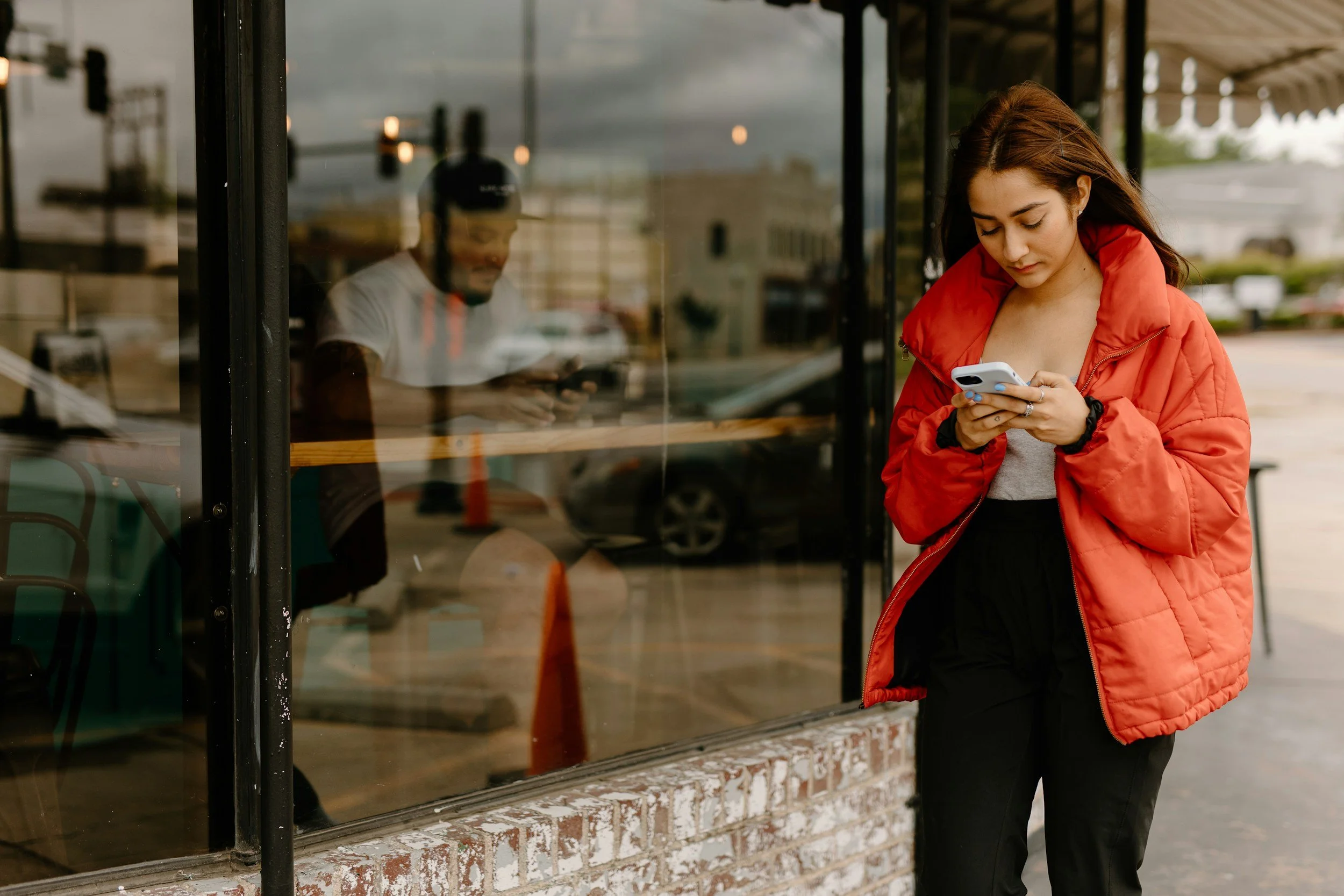woman in bright red puffer jacket walking along the street and reading text messages