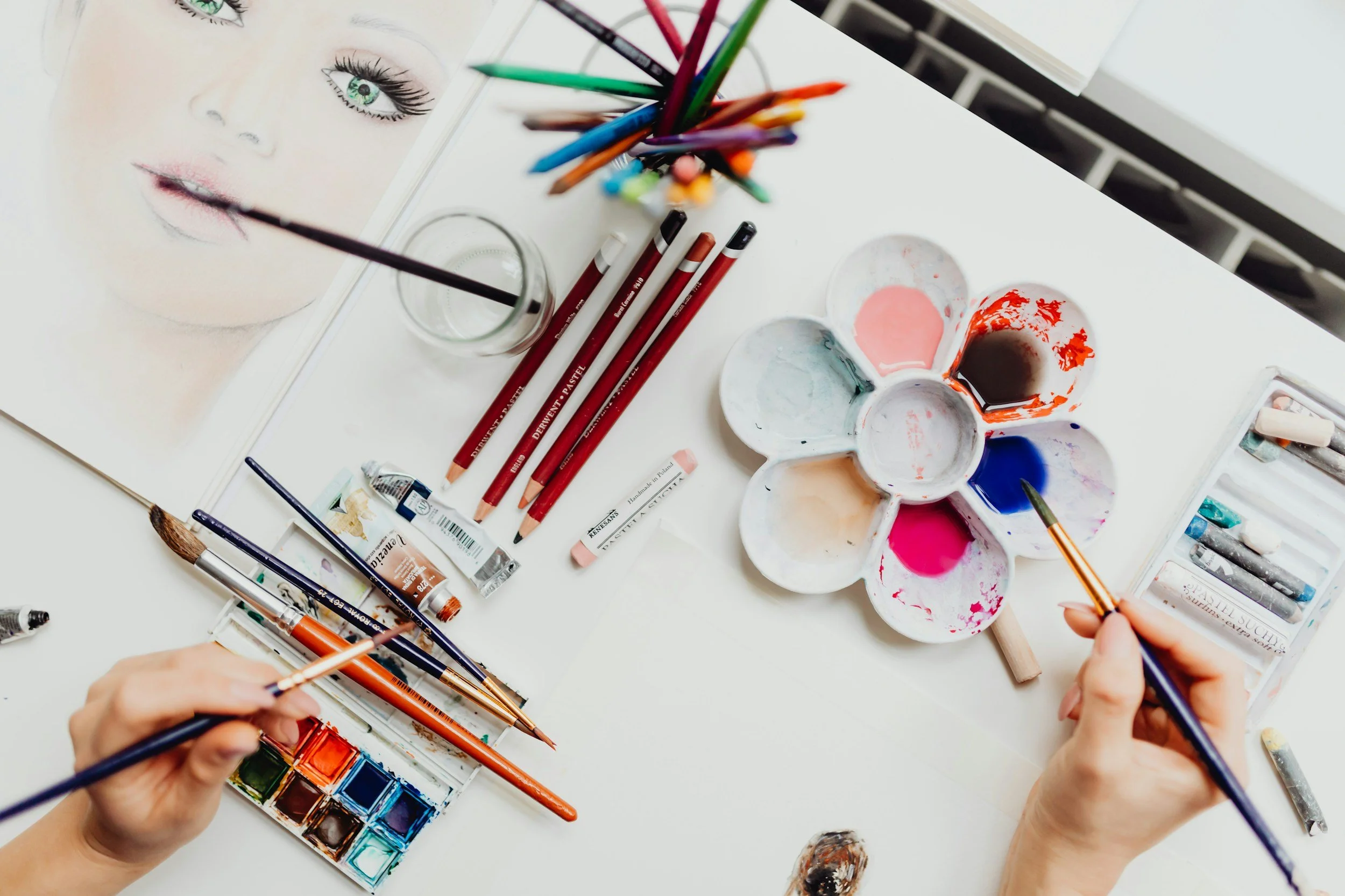 pencils and other art supplies and a woman's hand drawing fashion and makeup art