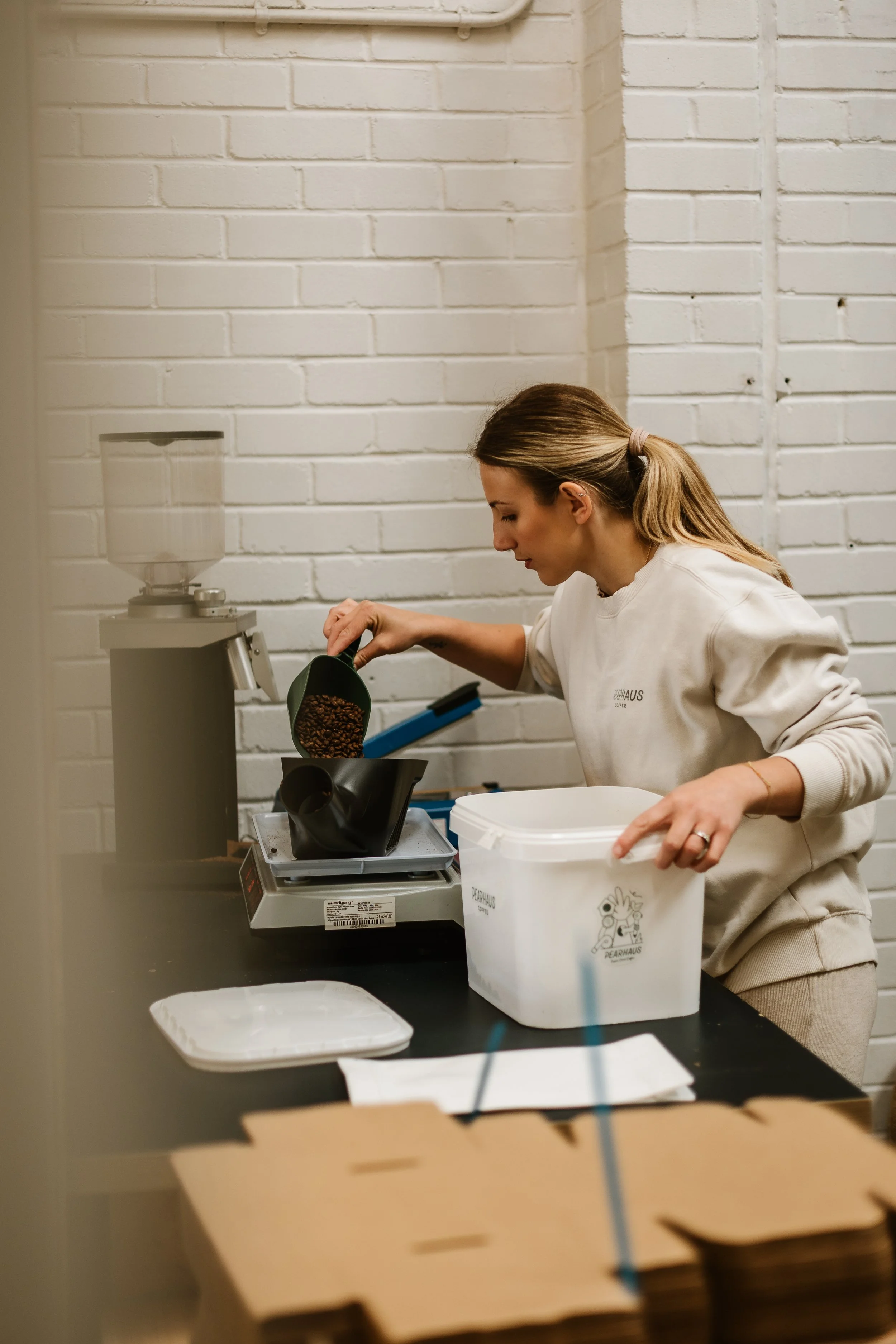 Charlie Co-founder is pouring coffee beans into a black coffee grinder at a work station with a white brick wall background.