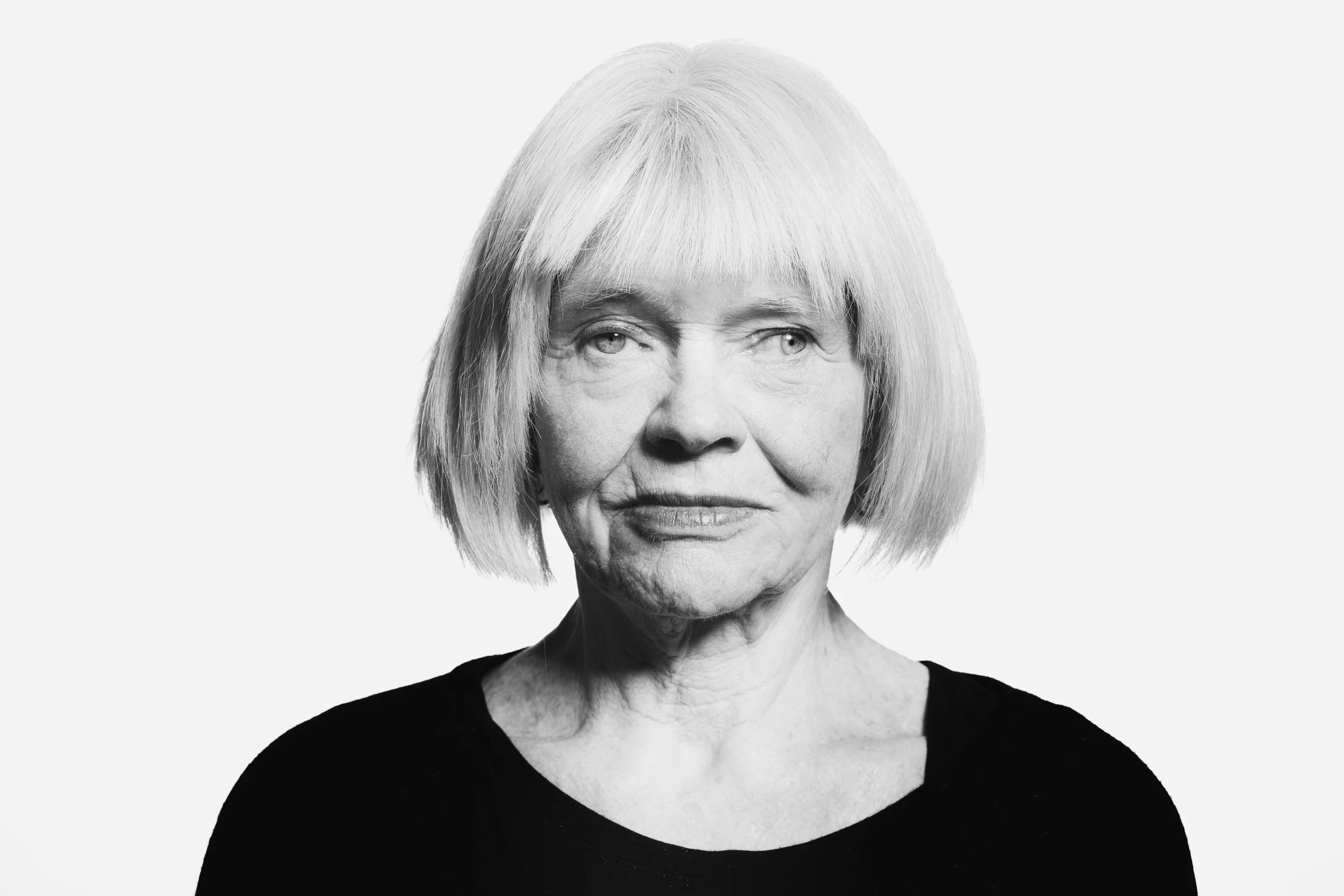 Black and white portrait of an elderly woman with short, straight hair, wearing a black top, looking slightly to the side.