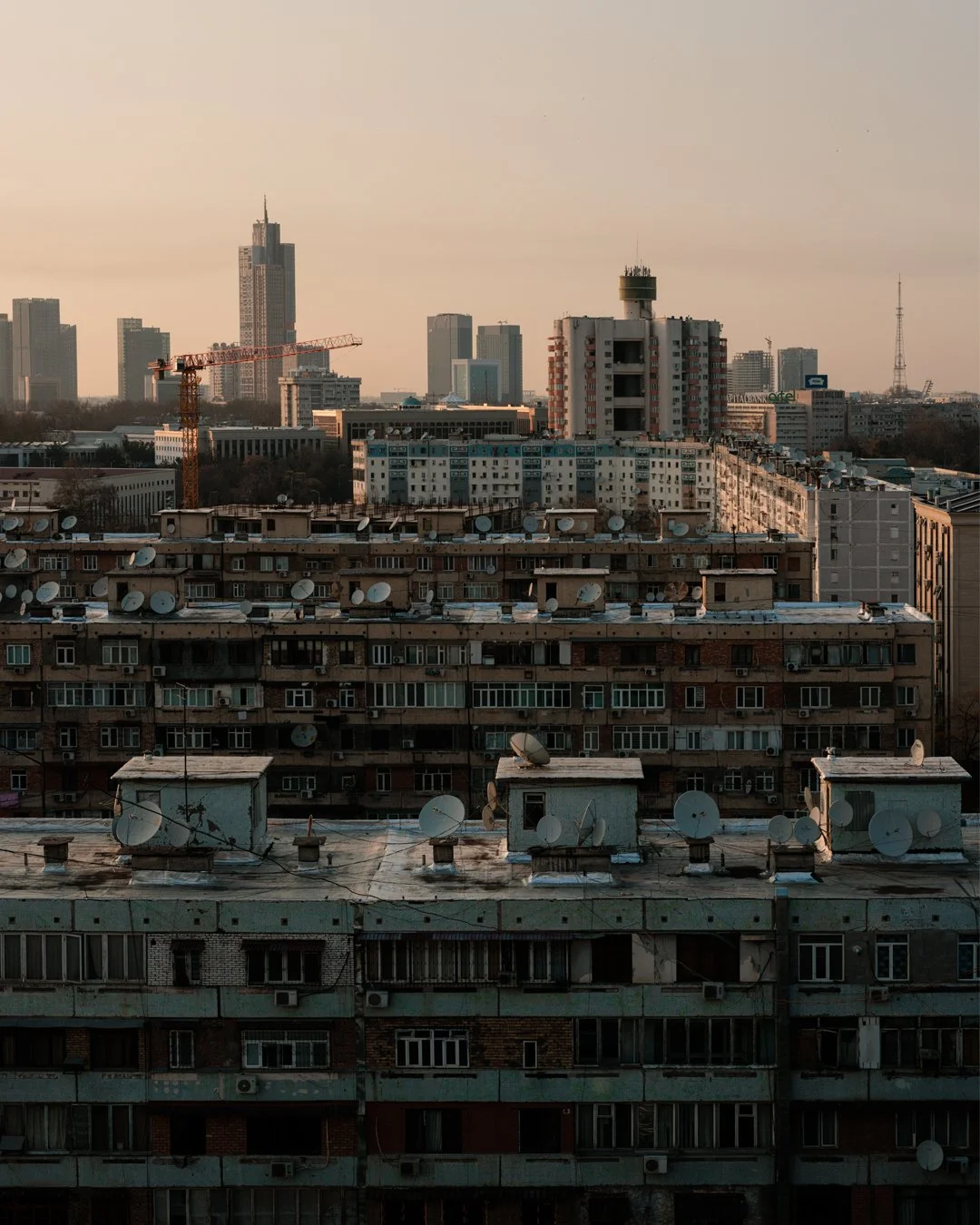 City skyline with numerous residential buildings and satellite dishes on rooftops during sunset.