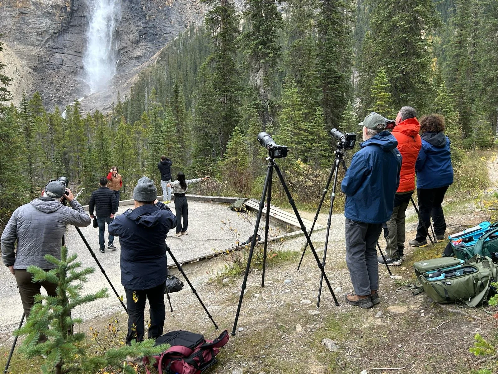 Group of people with cameras and tripods taking photos of a waterfall in a forested area.