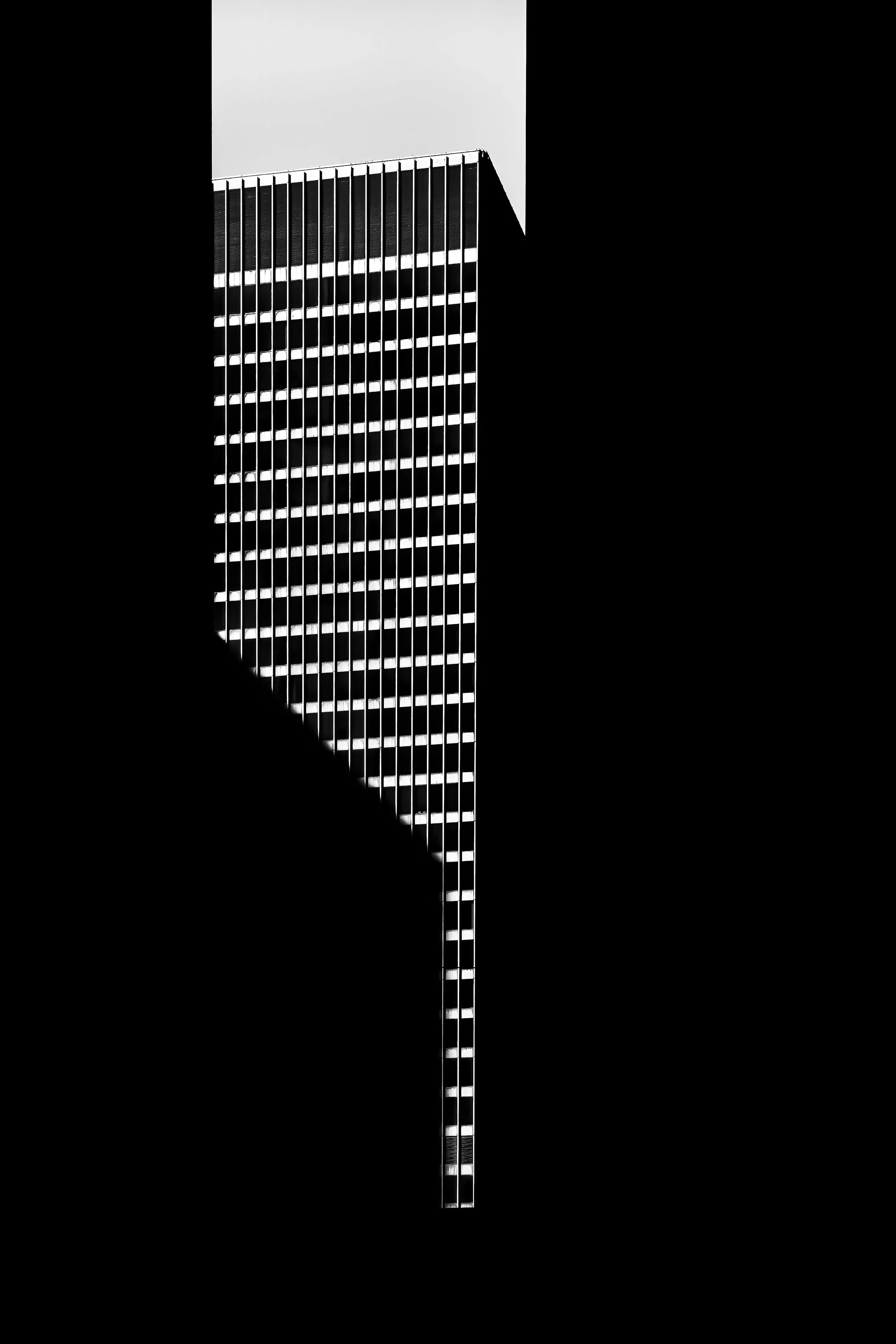 A tall modern skyscraper with a grid of windows, photographed from below against a stark sky.