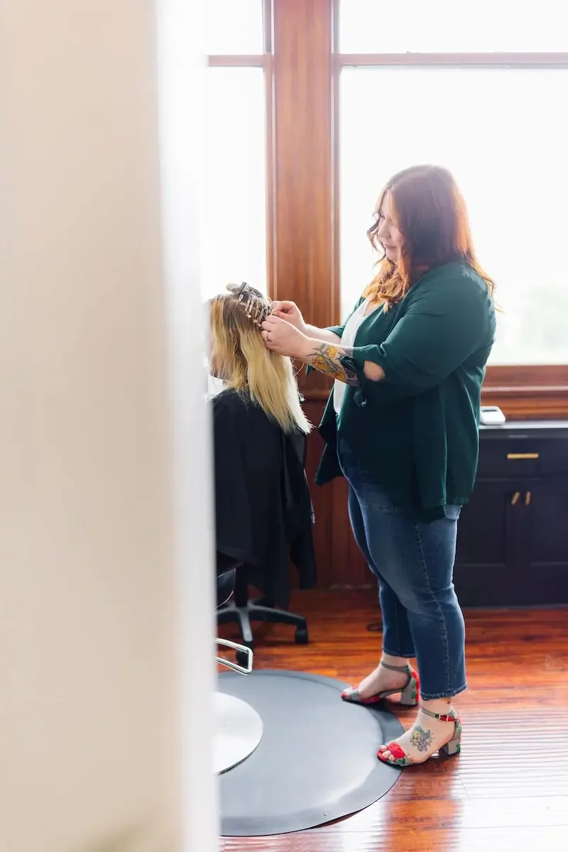 Hairstylist at The State Co in Livermore, CA styling a client’s blonde hair in a bright, modern salon with natural light and wood flooring.