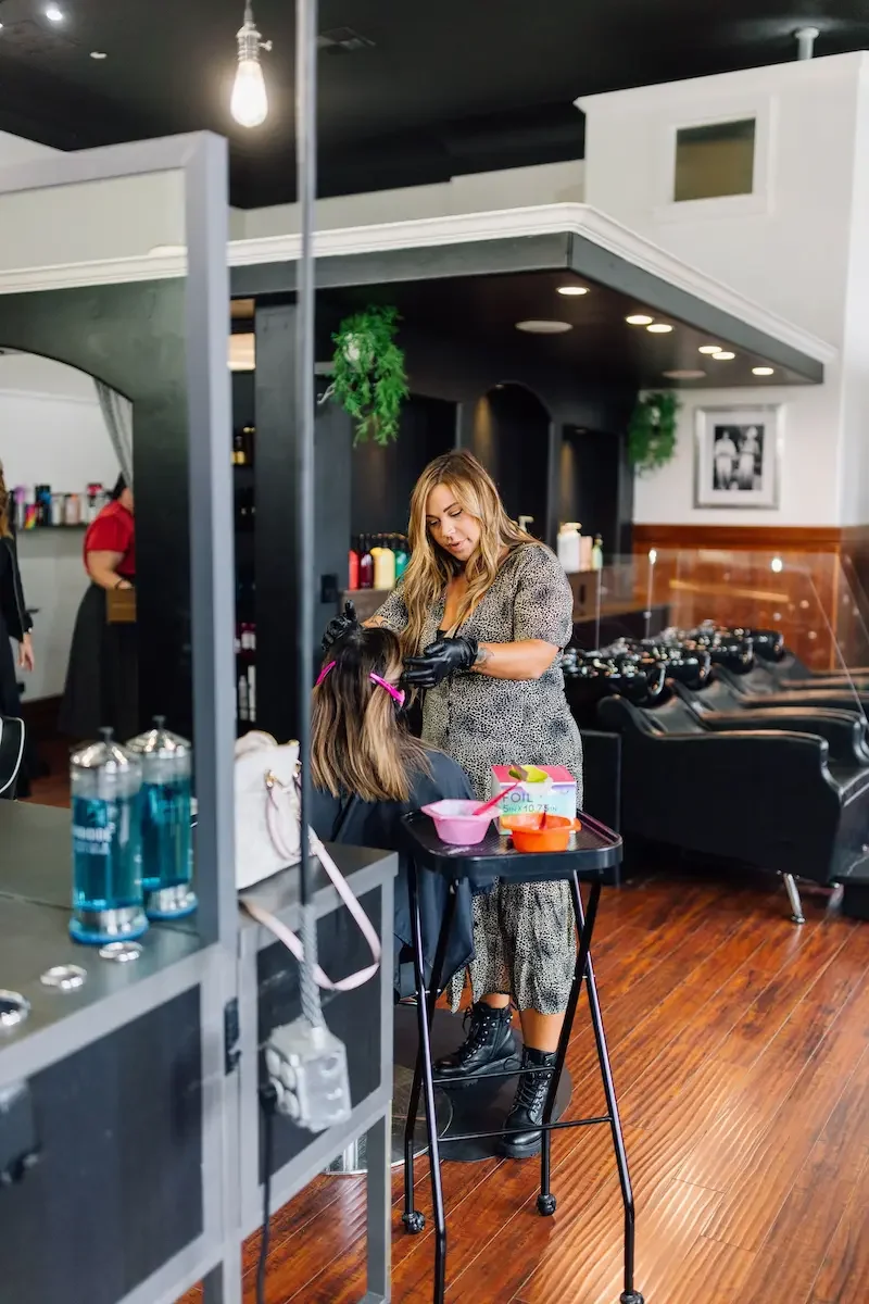 Guest enjoying a hair appointment at The State Co salon in Livermore, CA featuring modern décor, wooden floors, and hanging greenery.