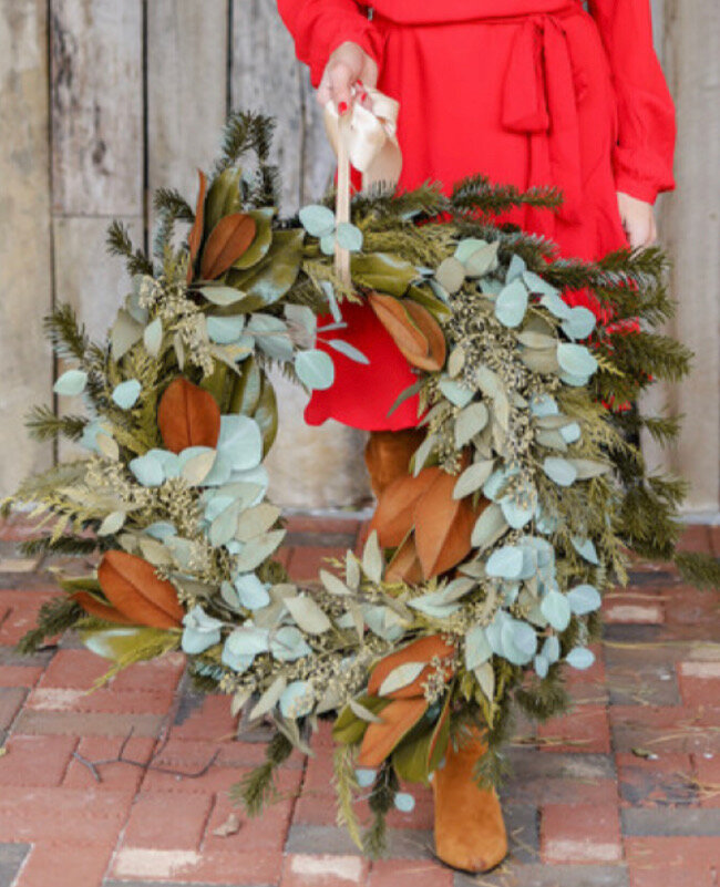 Person holding a large decorative wreath made of green and brown leaves.