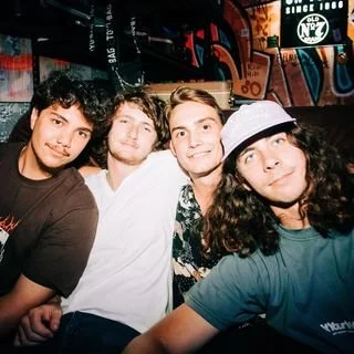 Four young adults posing together in a social setting with colorful artwork in the background.