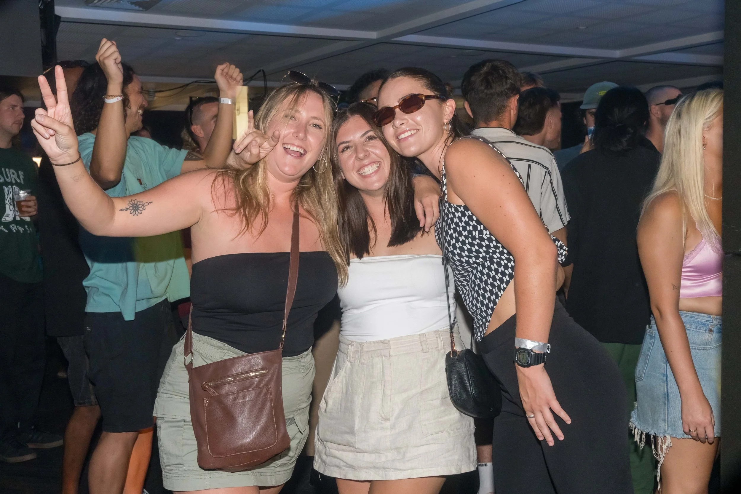 Three women smiling and dancing at a crowded party or music event.