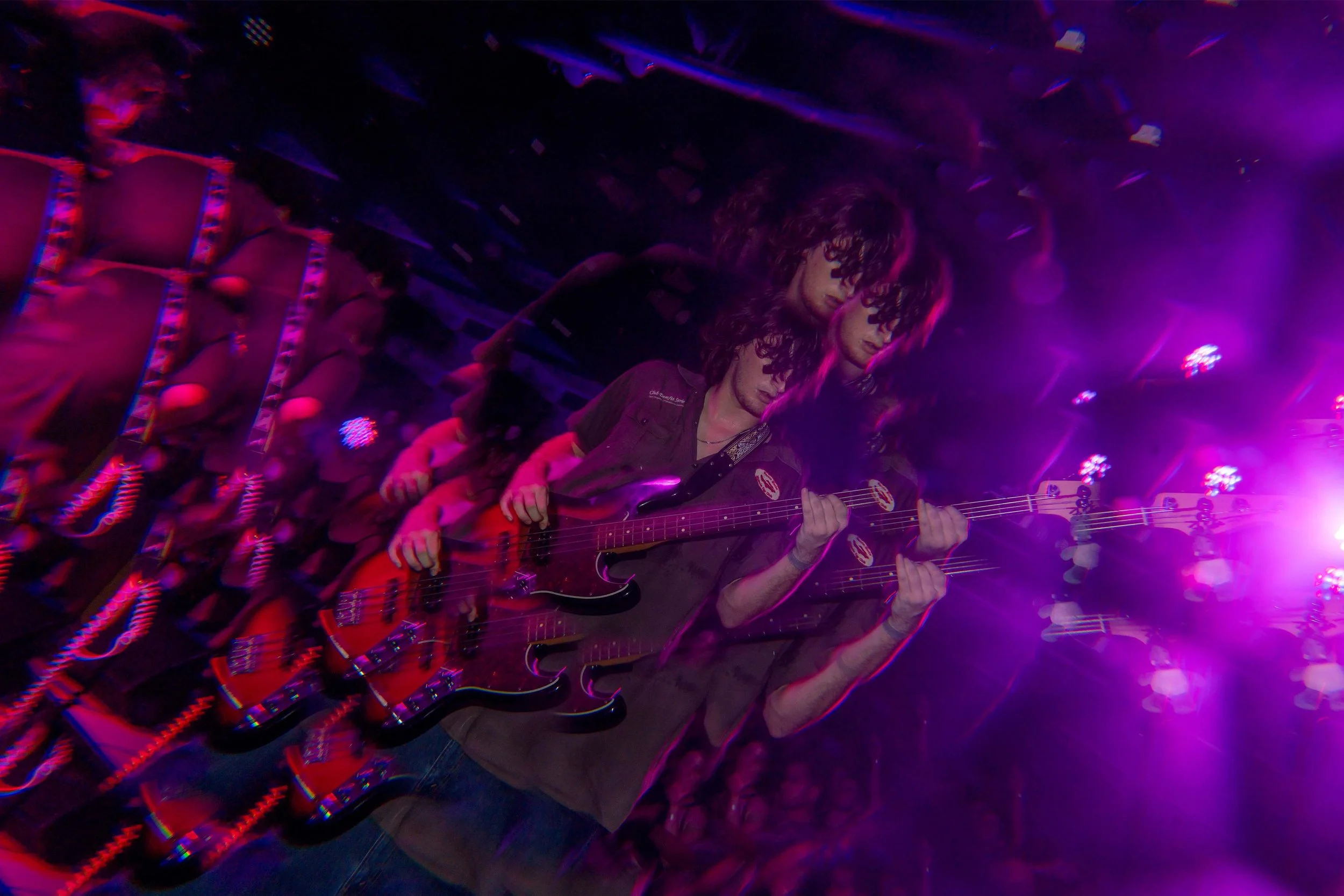 Multiple images of a male guitarist with curly hair playing an electric guitar in a dark, colorful stage setting with purple and pink lighting.