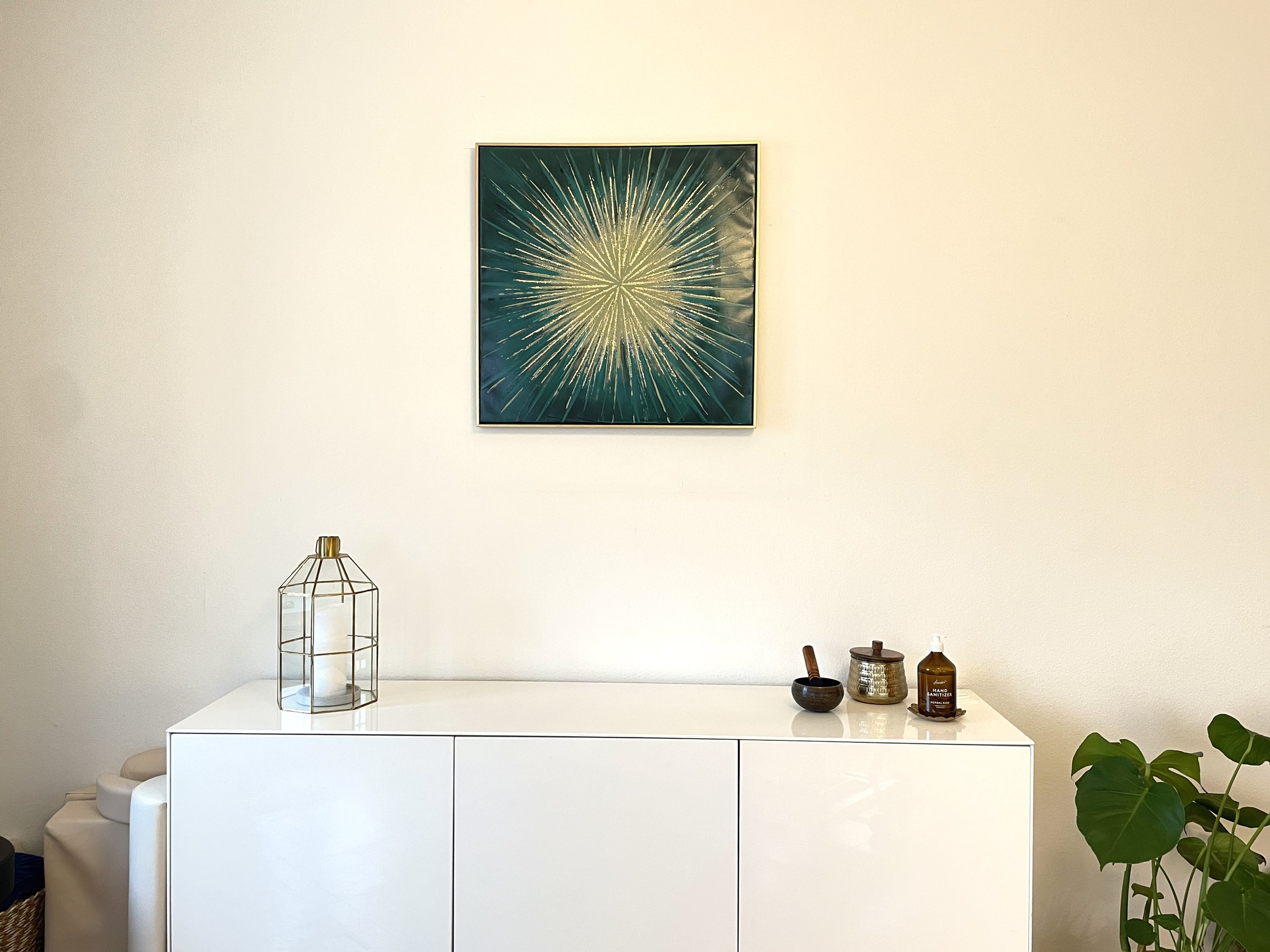 Weißes Sideboard mit Dekoration, Wandbild oben, Zimmerpflanze daneben.