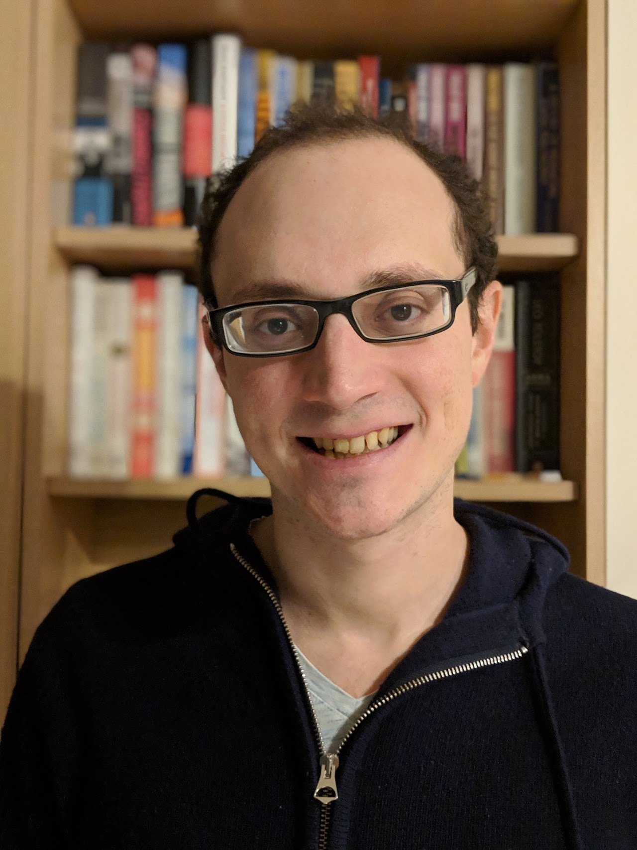 Joel Z. Leibo poses for a headshot in front of a bookcase wearing glasses