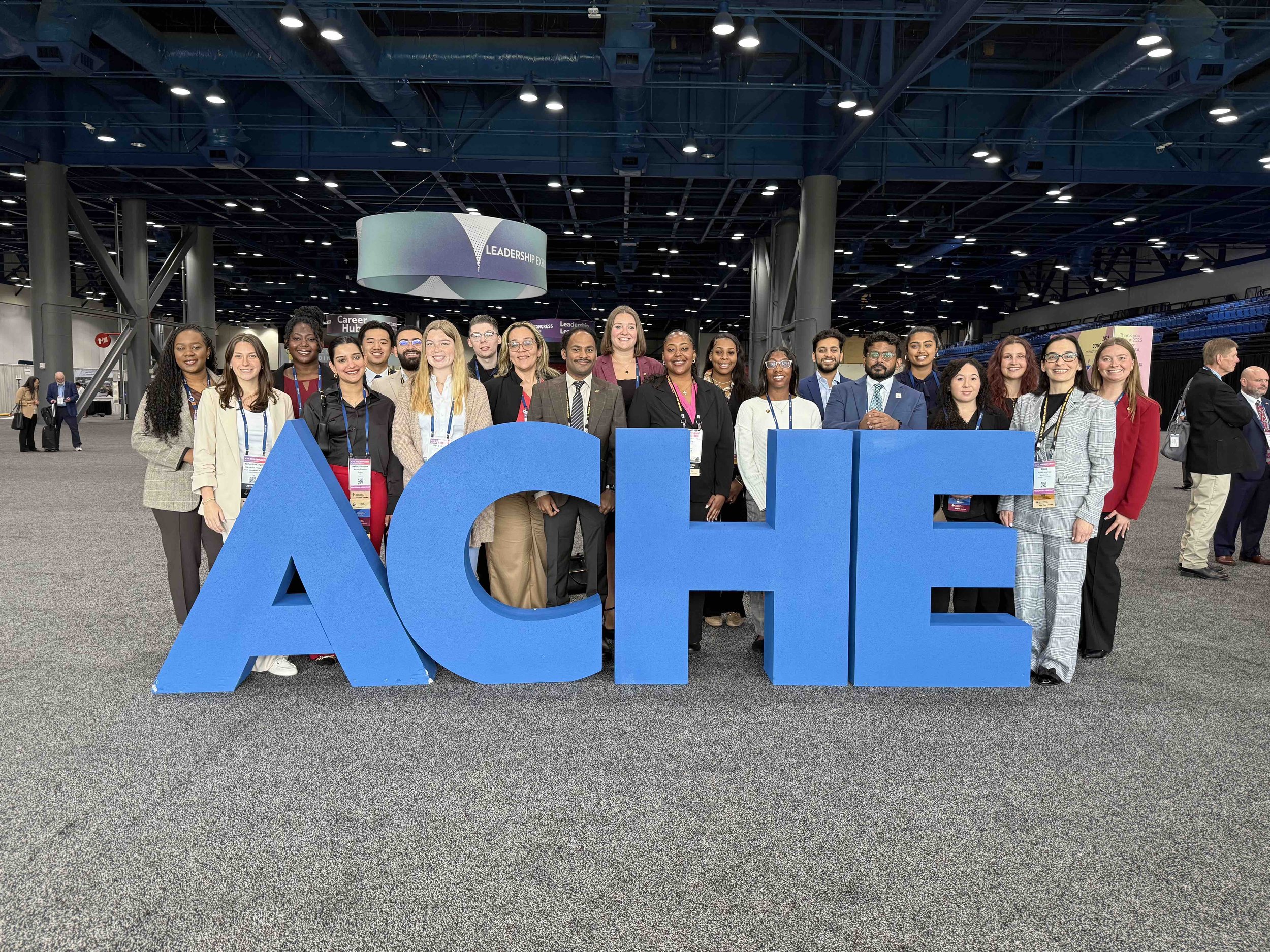 Group of diverse people smiling behind large blue letters spelling 'ACHE' at a conference or event.