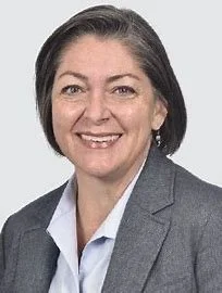 Portrait of a woman with shoulder-length dark hair, wearing a gray blazer and white shirt, smiling.