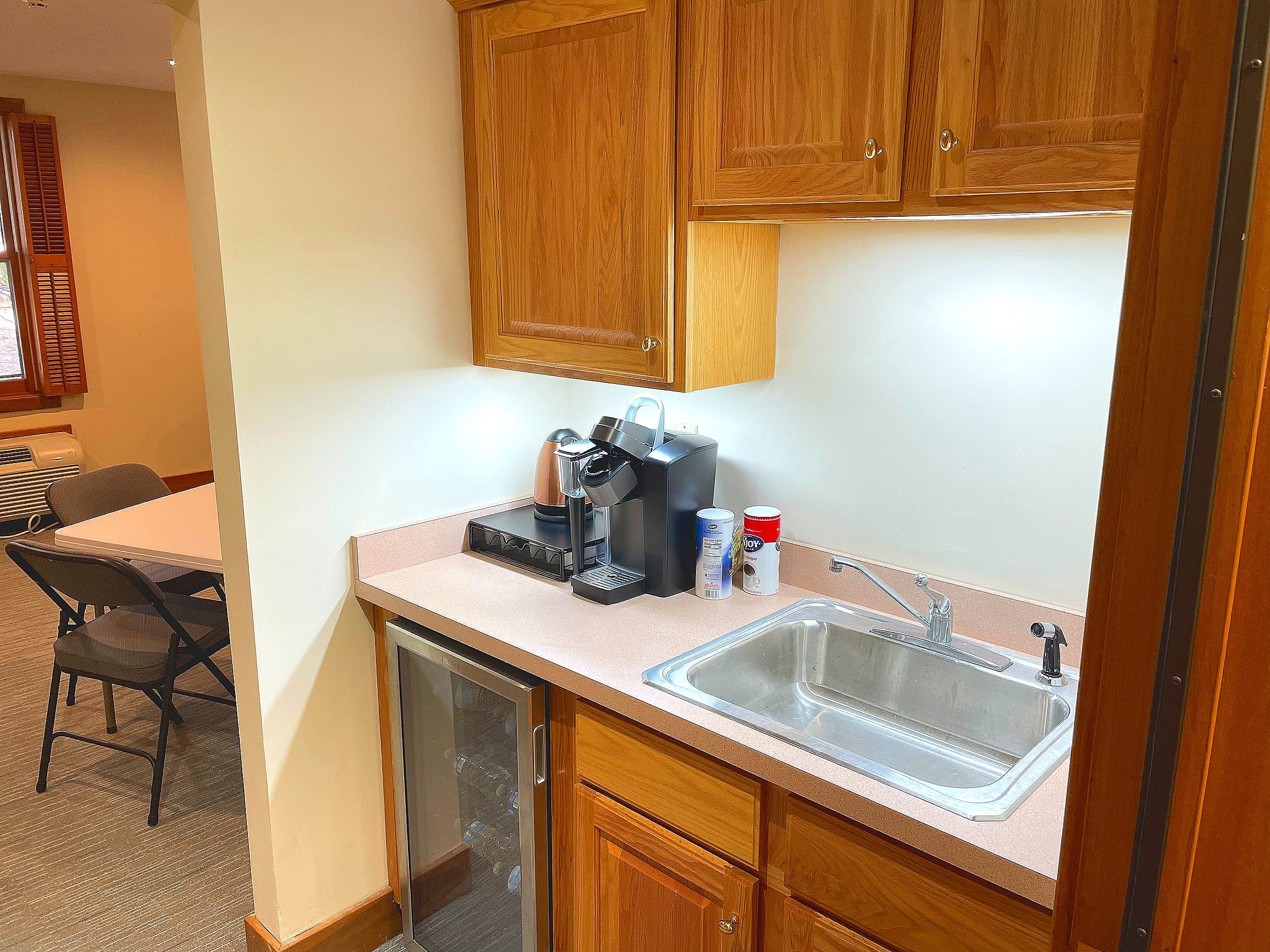   The room’s kitchenette has a small refrigerator, sink, and coffee maker. There is a large space for coats opposite the kitchen counter.  