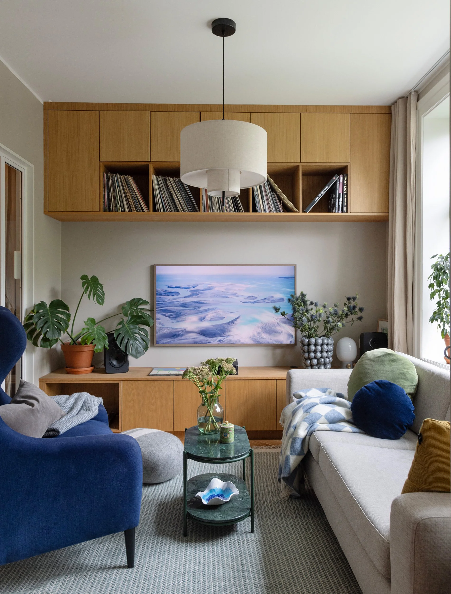 Stue med plassbygget eikeinnredning for TV, oppbevaring og platesamling.