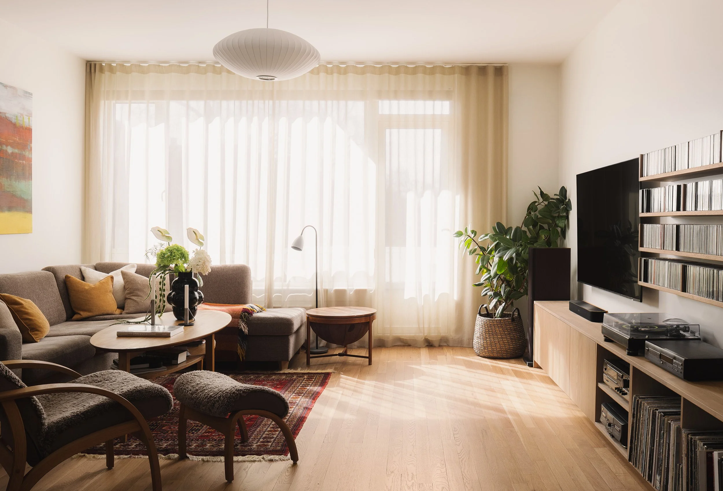 Stue med eikeinnredning for TV, vinyl og musikksamling samt store vindusflater.