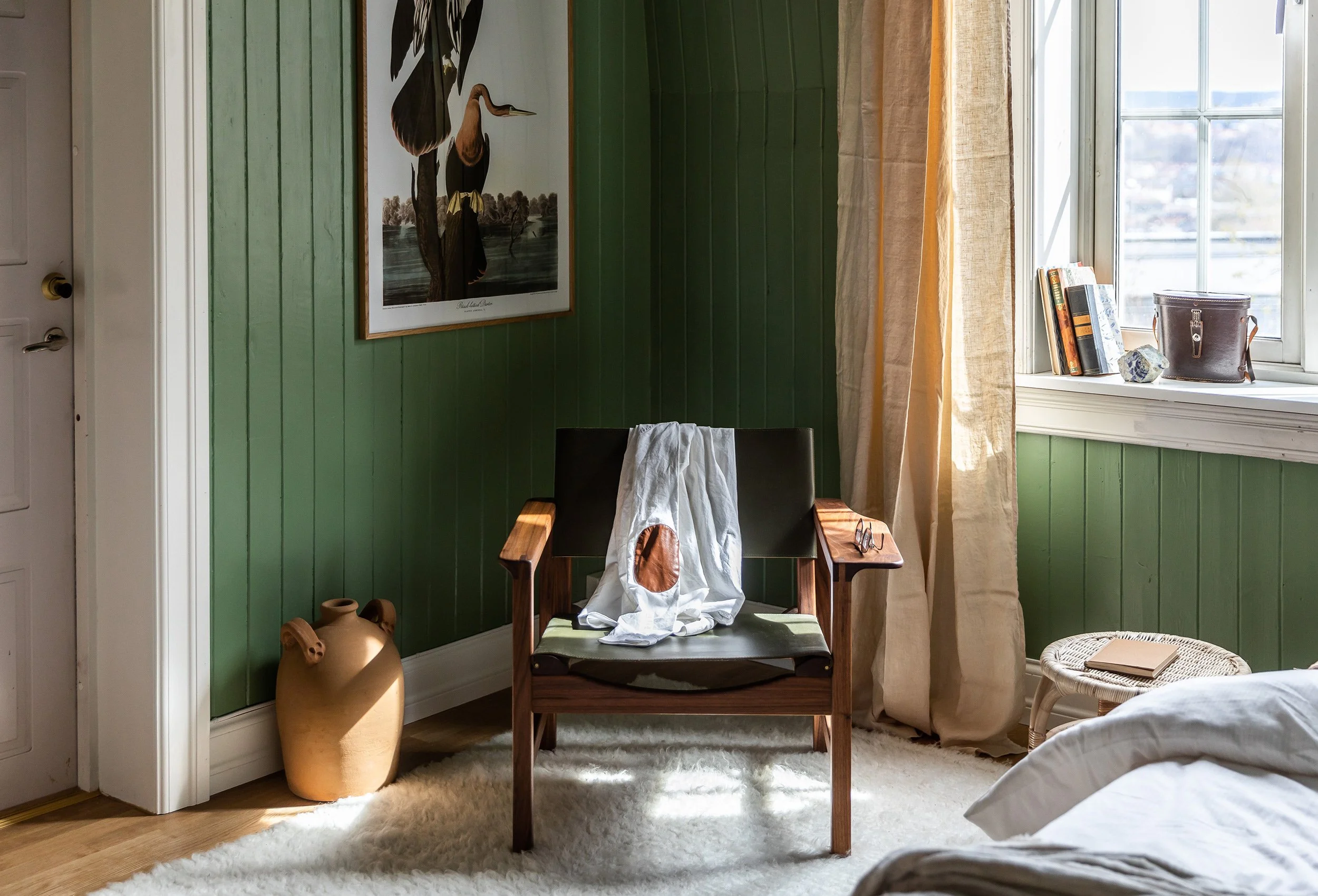 Soverom med grønt panel, vintage lenestol og dagslys fra bakgården.