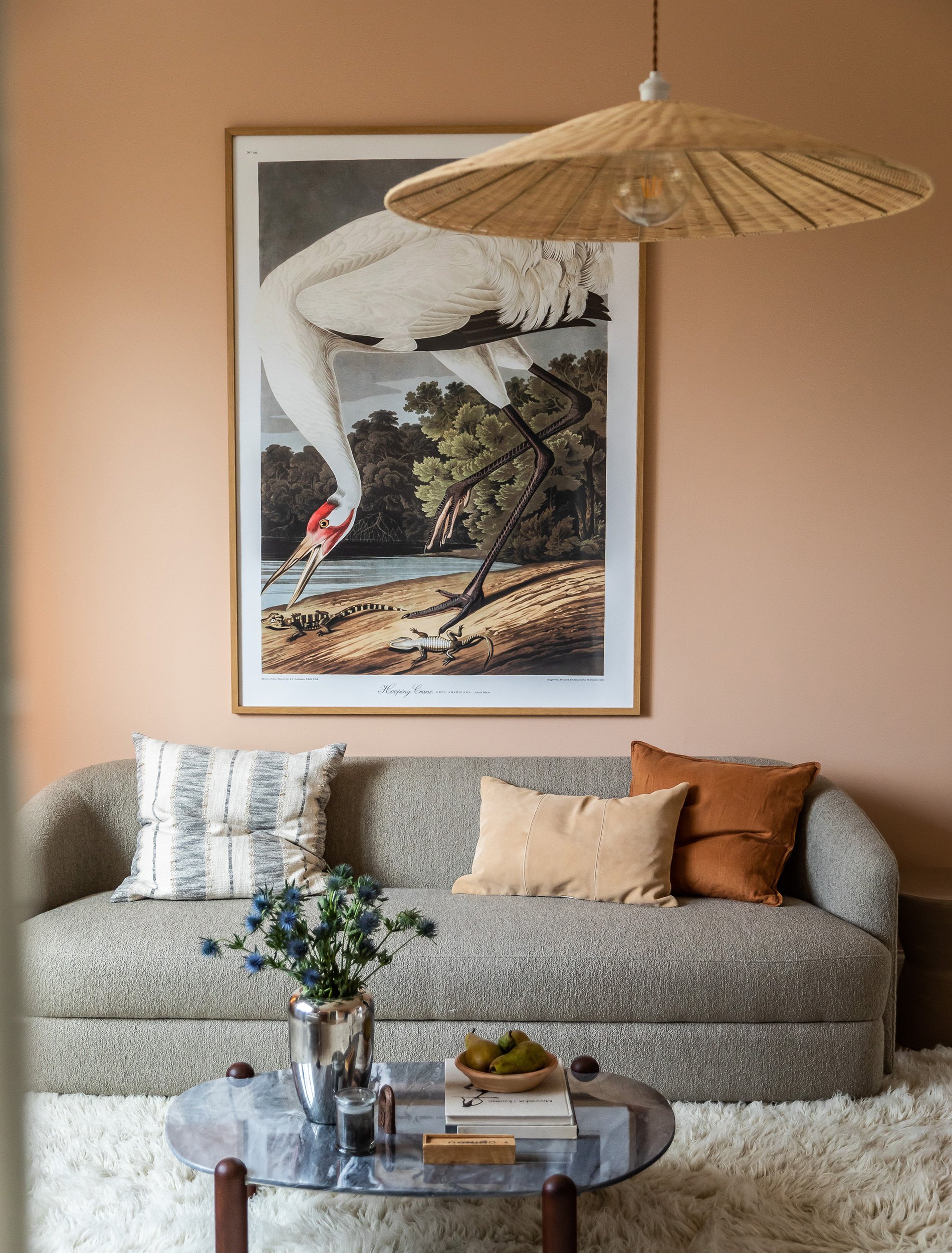 Sofa og salongbord mot varm veggfarge og botanisk kunst i stuen.