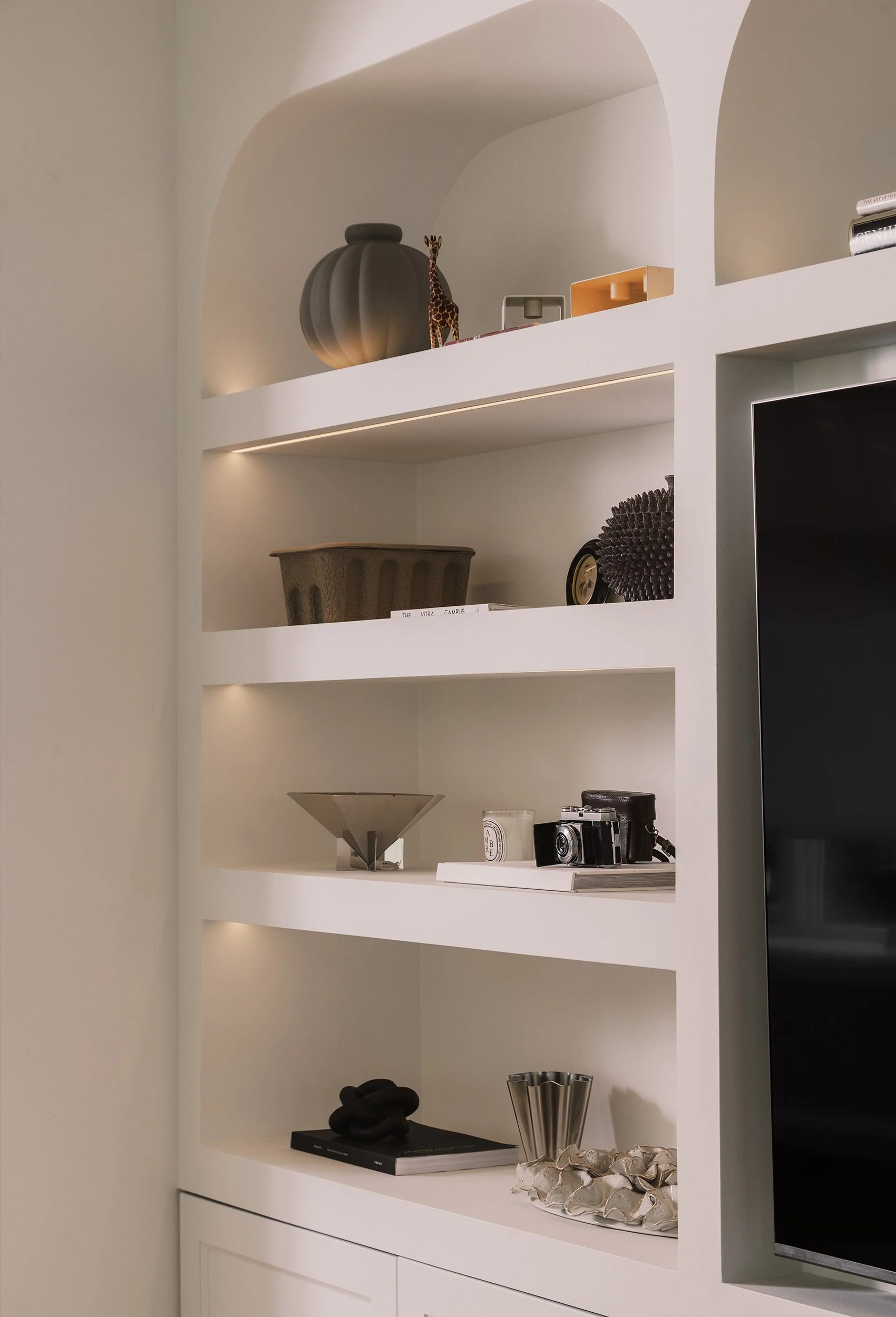 Detalj av plassbygget bokhylle med buede nisjer og integrert belysning.