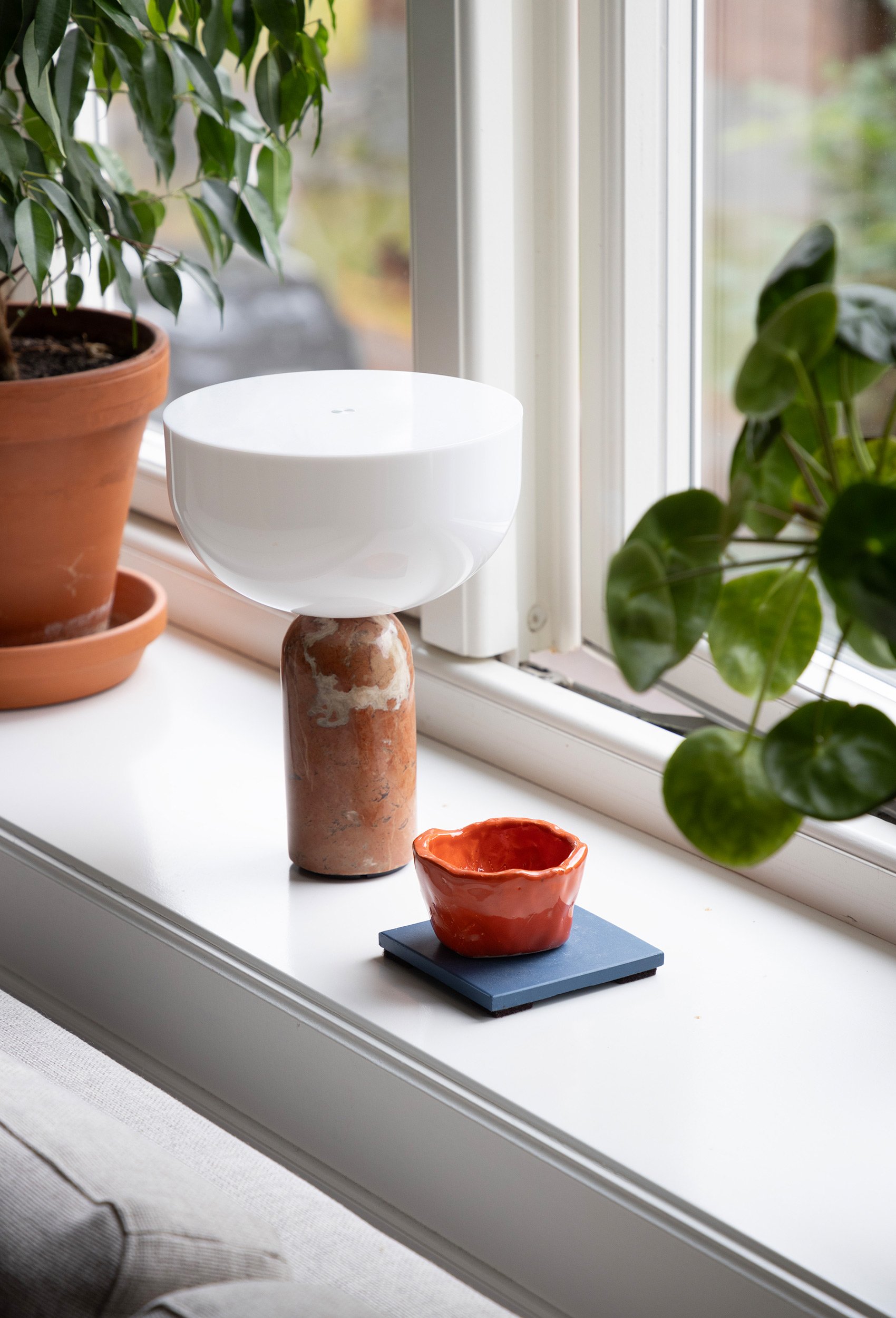 Detalj av keramikk og grønne planter i vinduskarmen i stuen.